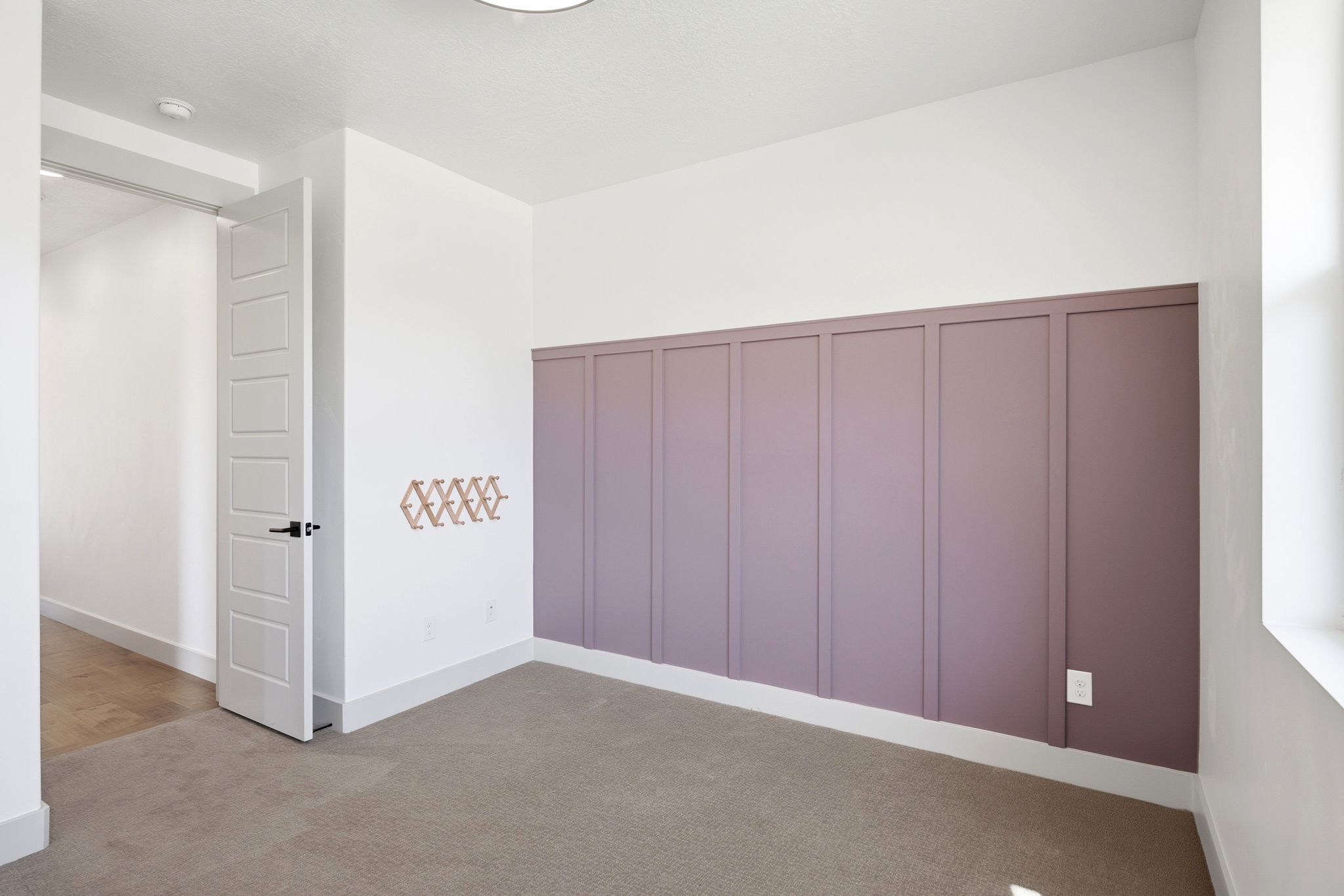 Room featuring a striking accent wall with vertical paneling, light-colored carpeting, and a modern flush-mount ceiling light