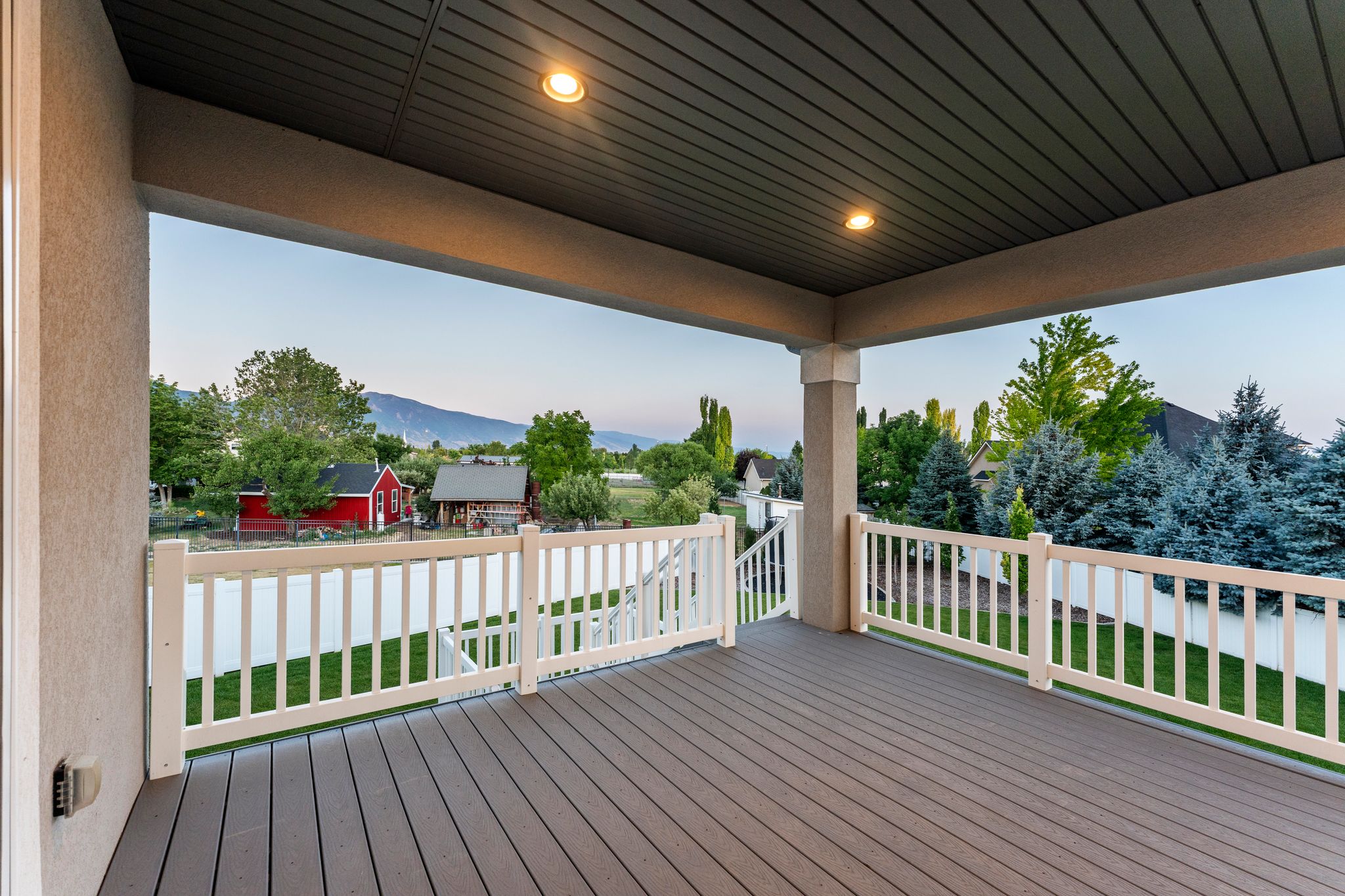 Covered outdoor deck featuring composite decking, white railing, recessed lighting, and stucco columns