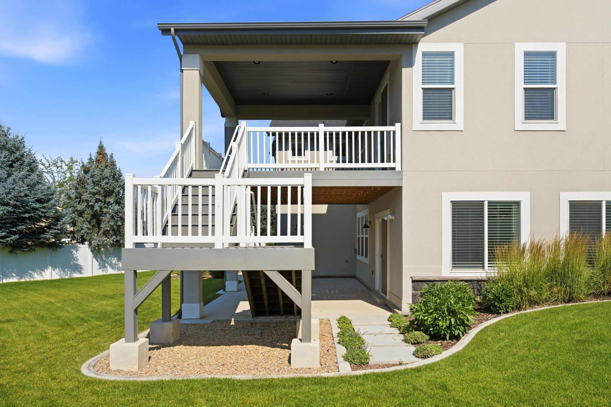 Multi-level deck and patio featuring a covered upper deck, white railing, exterior staircase, concrete paver pathway, and surrounding landscaping
