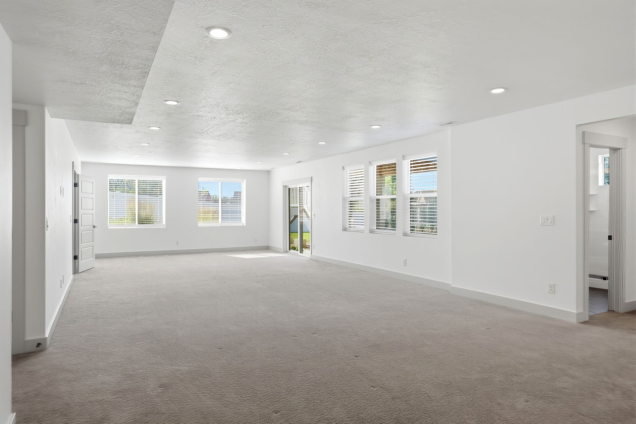 Expansive carpeted room featuring multiple windows, recessed lighting, and a neutral color palette