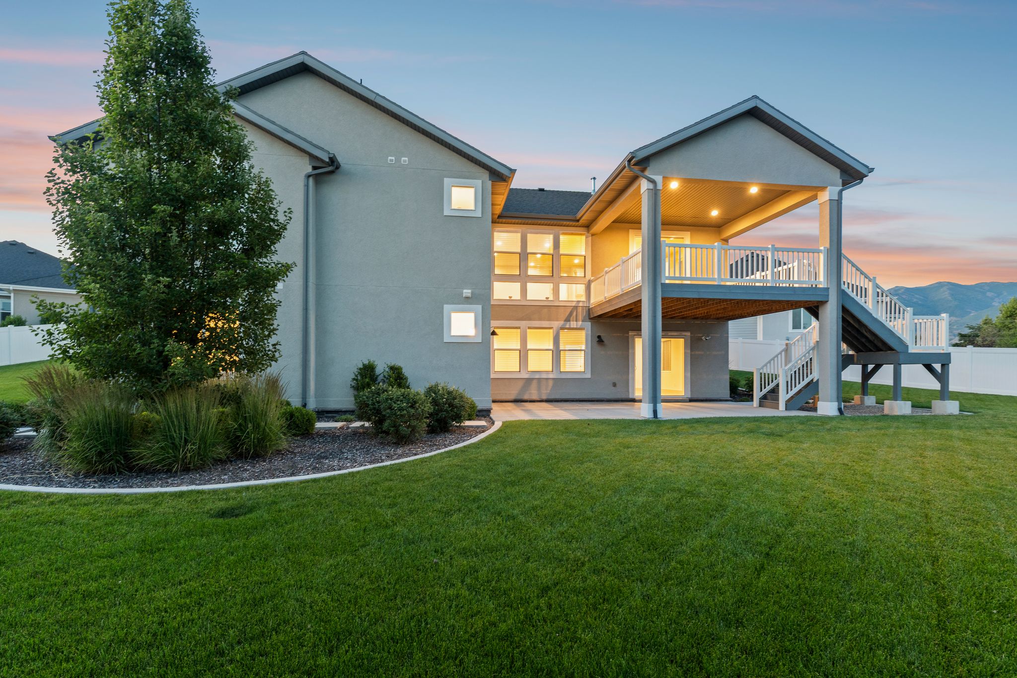 Expansive rear exterior featuring a covered deck with white railing, a ground-level patio, and a manicured lawn