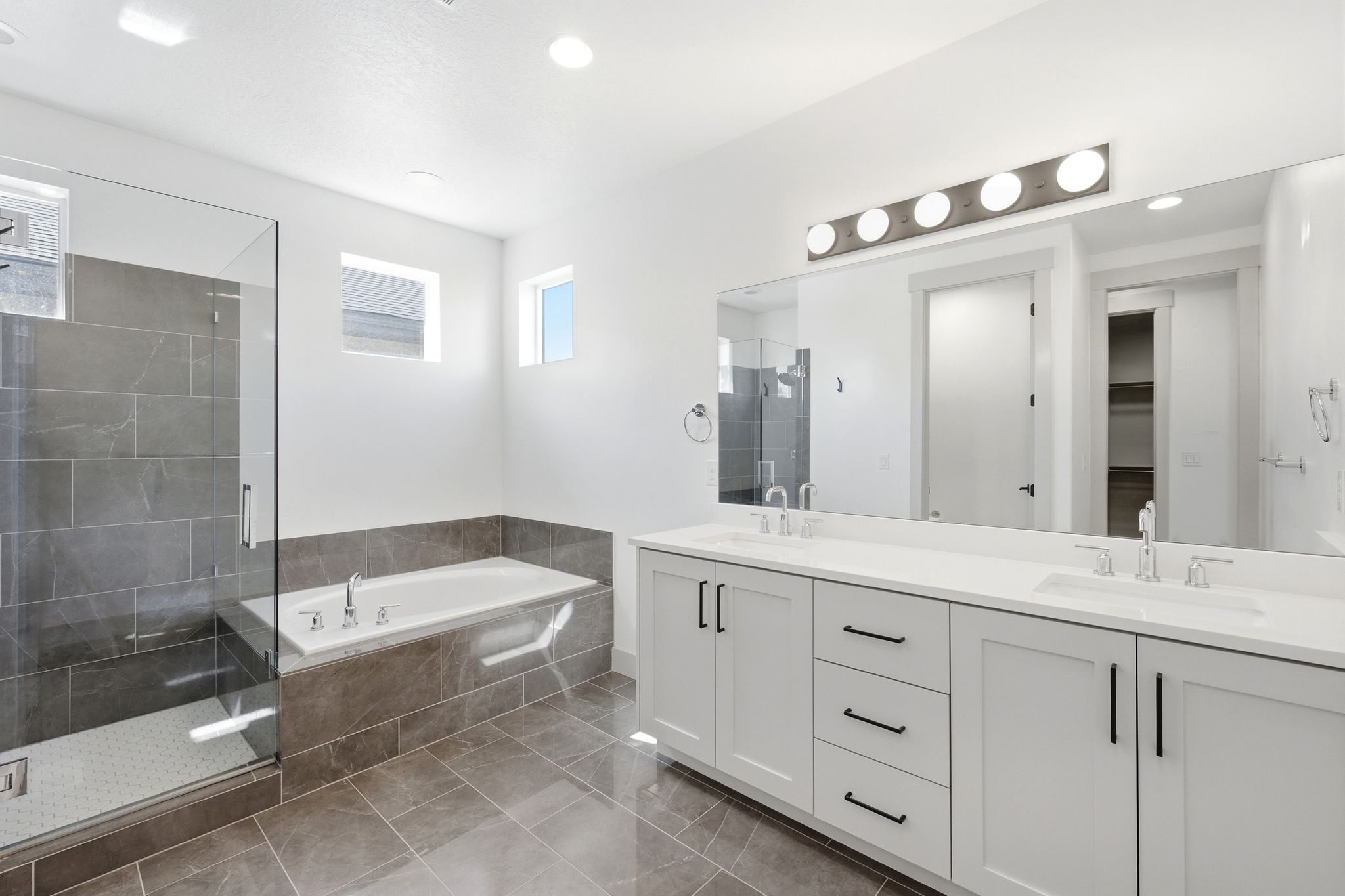 Spacious bathroom featuring a double vanity with white cabinetry, a large frameless mirror, and a five-light fixture