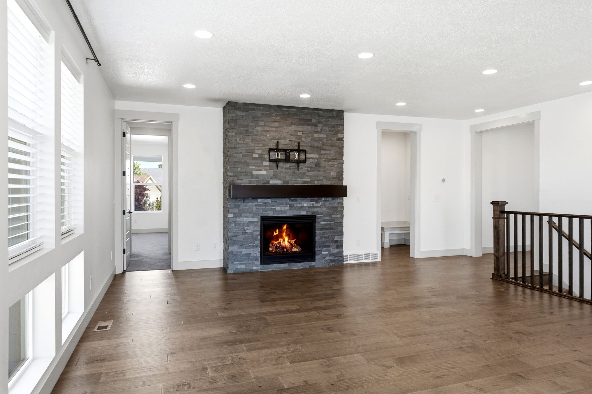 Spacious living area featuring a stacked stone fireplace with a dark wood mantel, recessed lighting, and wood-finish flooring