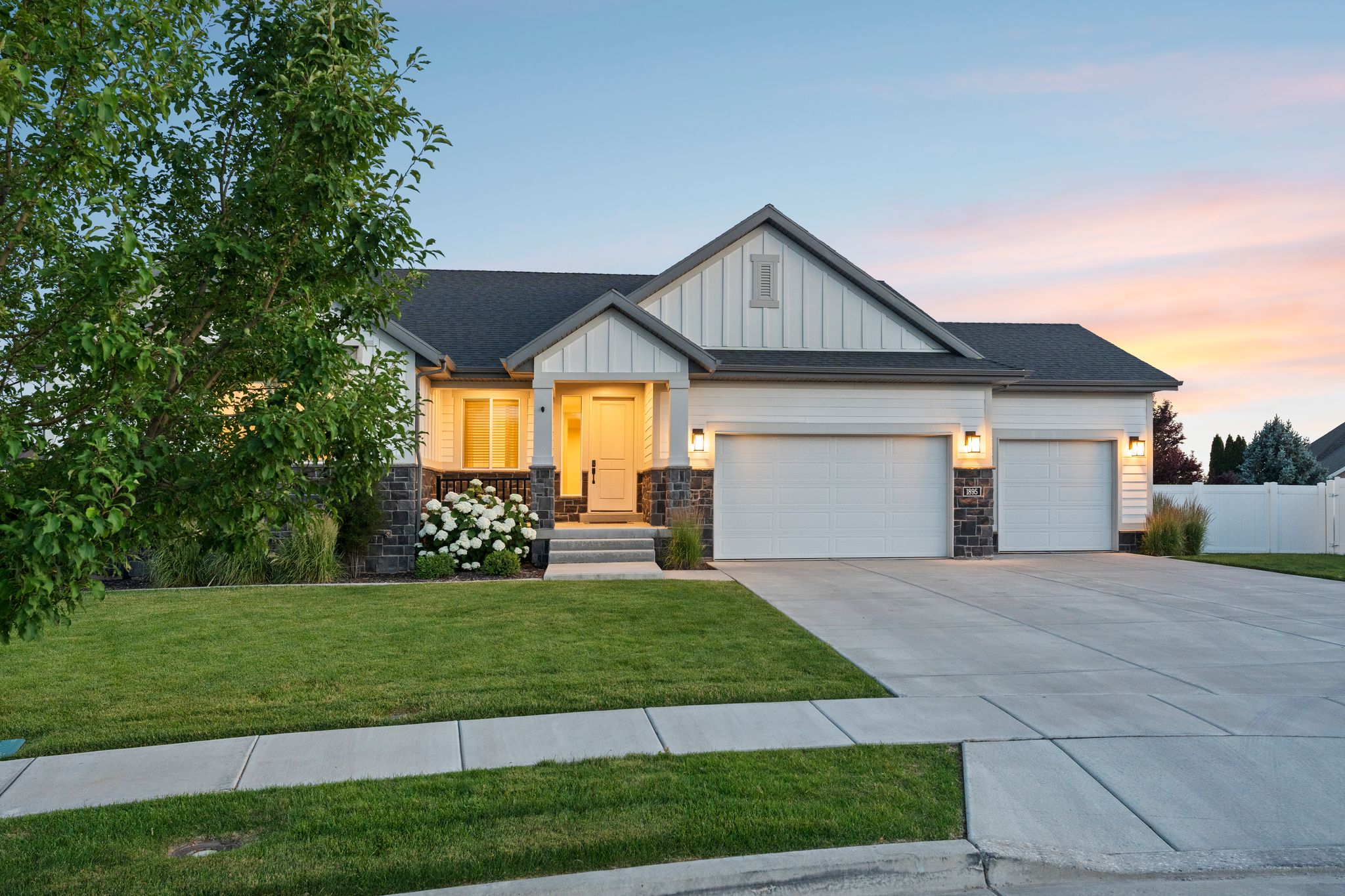 Ranch-style exterior with board and batten siding, stone accents, a dark shingle roof, and a two-car garage