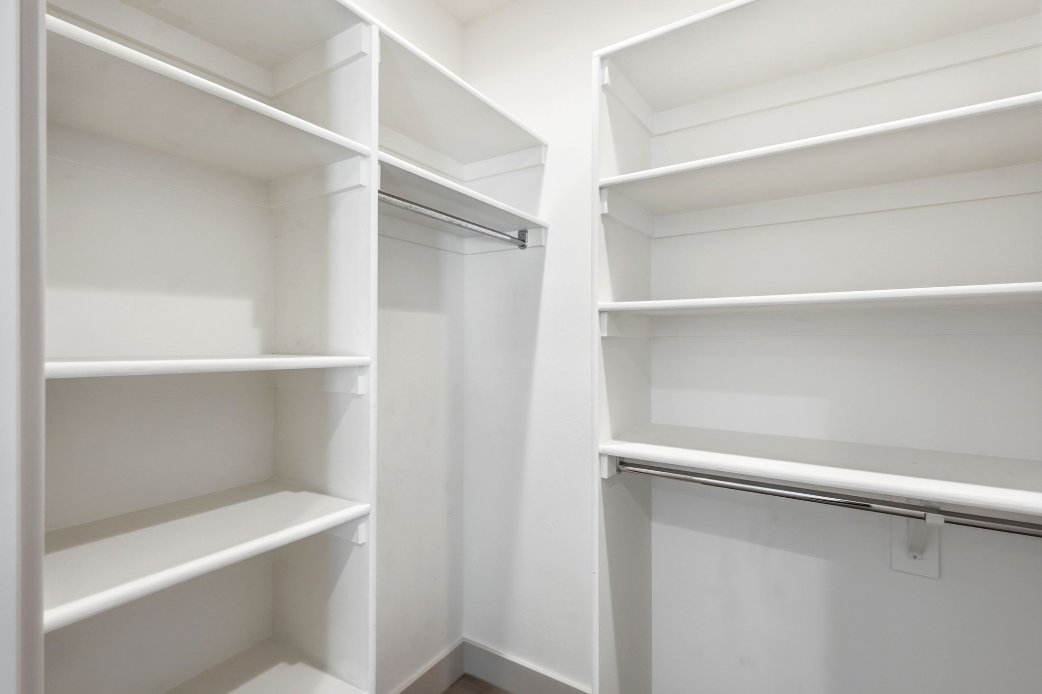 Walk-in closet featuring white built-in shelving units and metal hanging rods