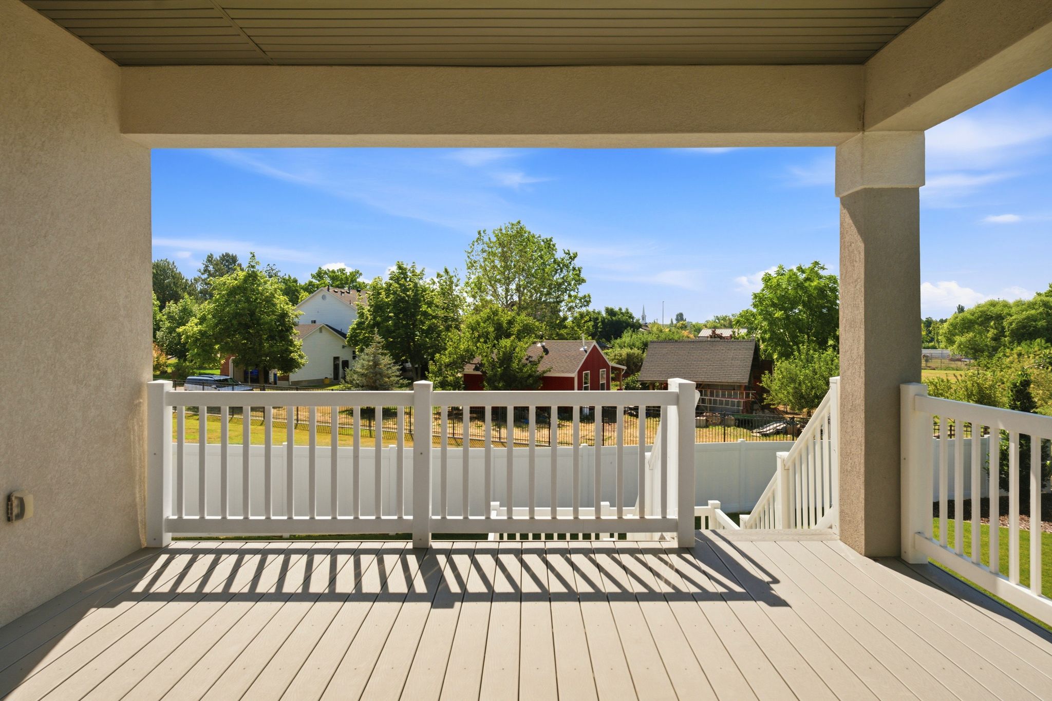Spacious covered deck featuring composite decking, white railing system, and stucco columns
