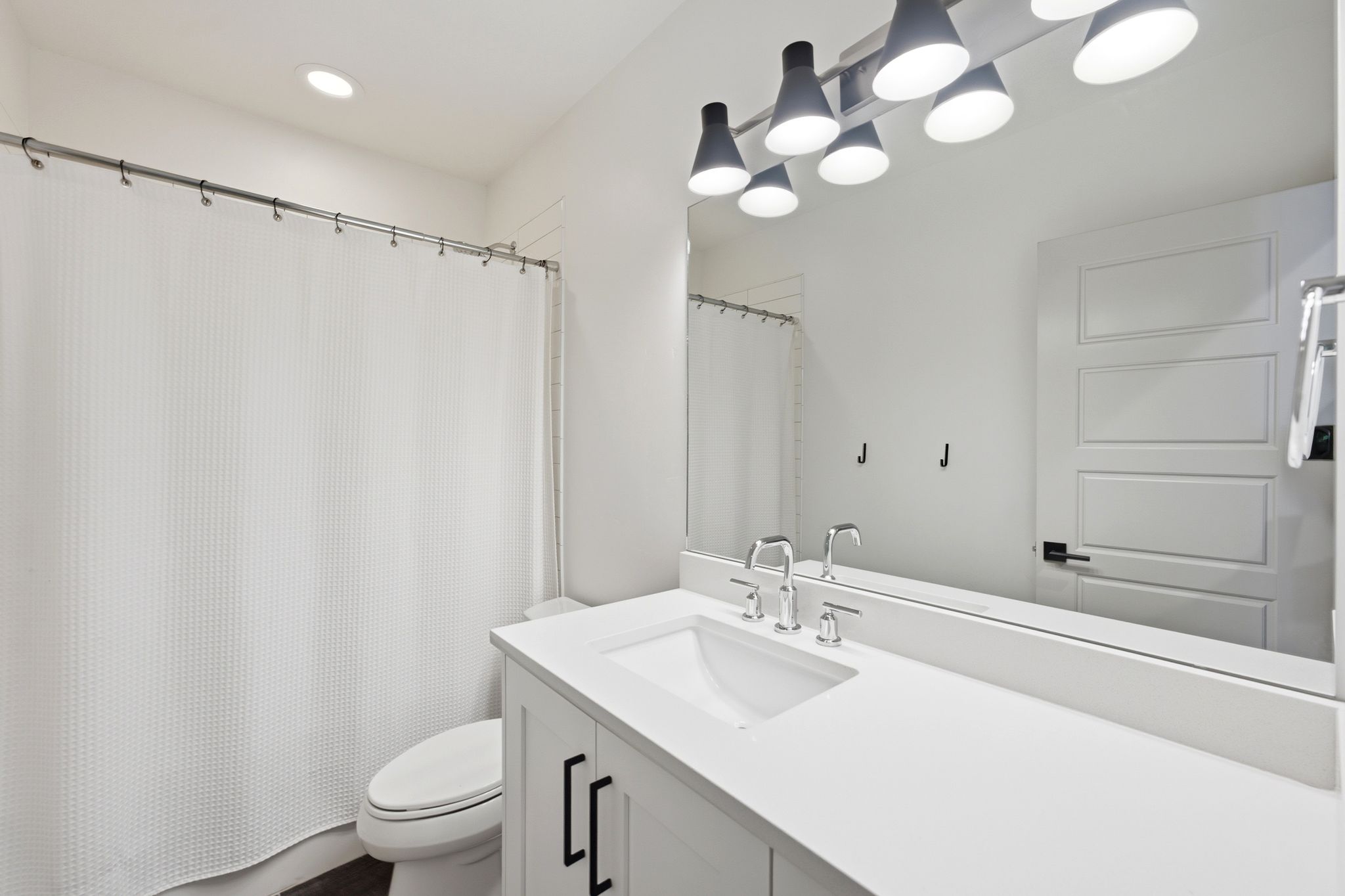 Contemporary bathroom featuring a single vanity with a white countertop and integrated sink, chrome faucet, and matte black cabinet hardware