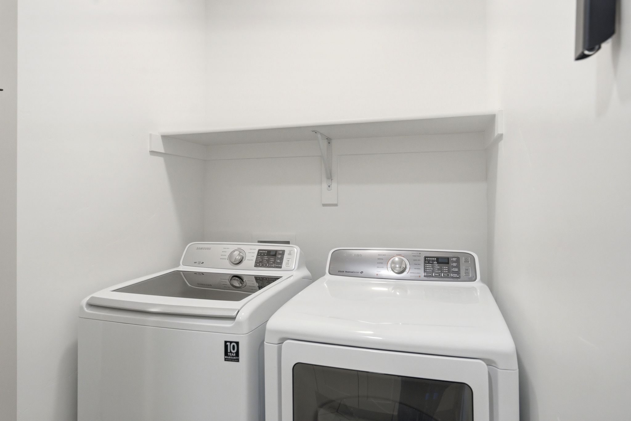 Dedicated laundry area featuring a white wall shelf, white walls, and a white ceiling