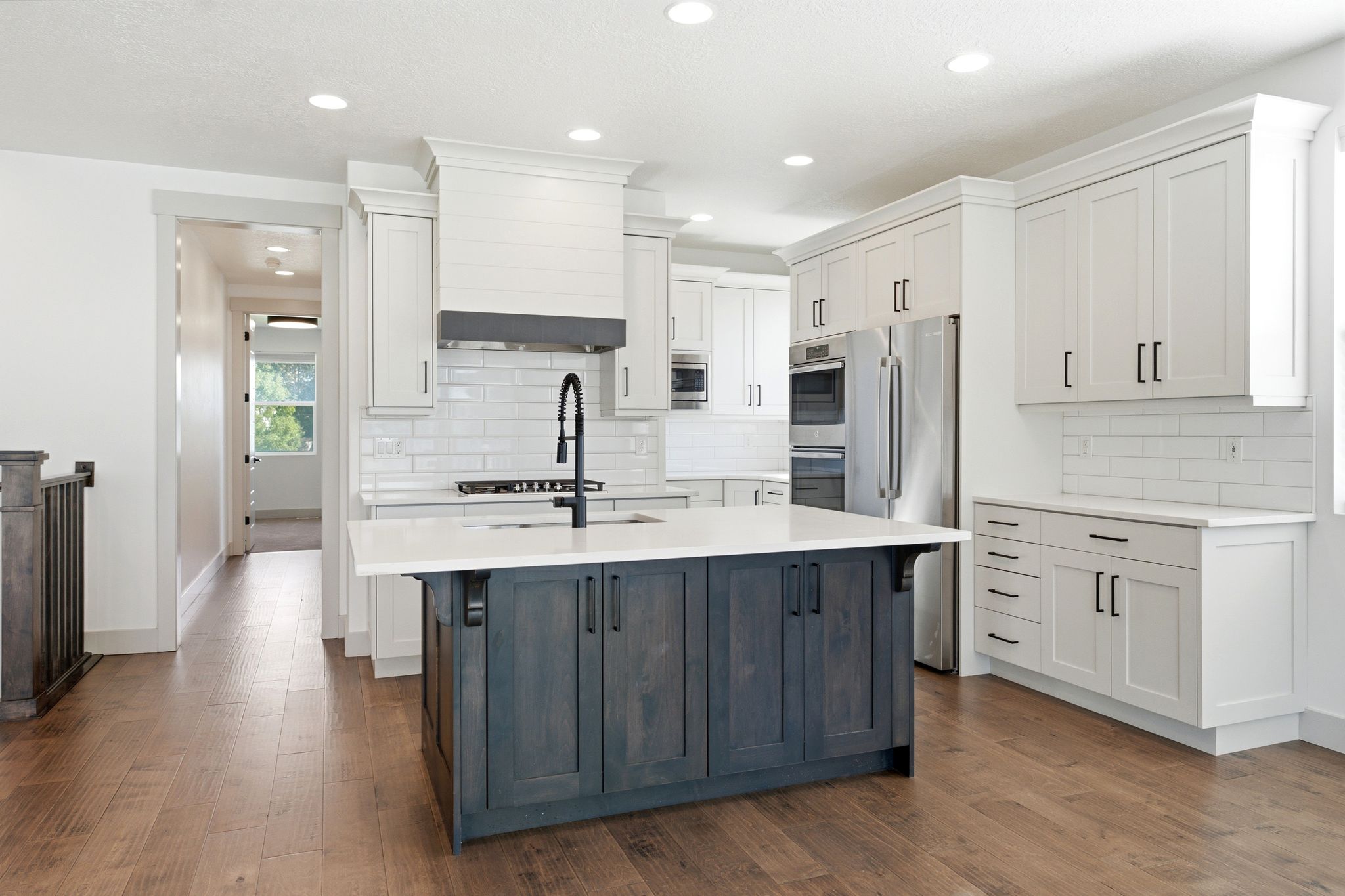 Gourmet kitchen featuring a two-tone island with a quartz countertop, stainless steel appliances, white shaker cabinetry, subway tile backsplash, and wood-finish flooring