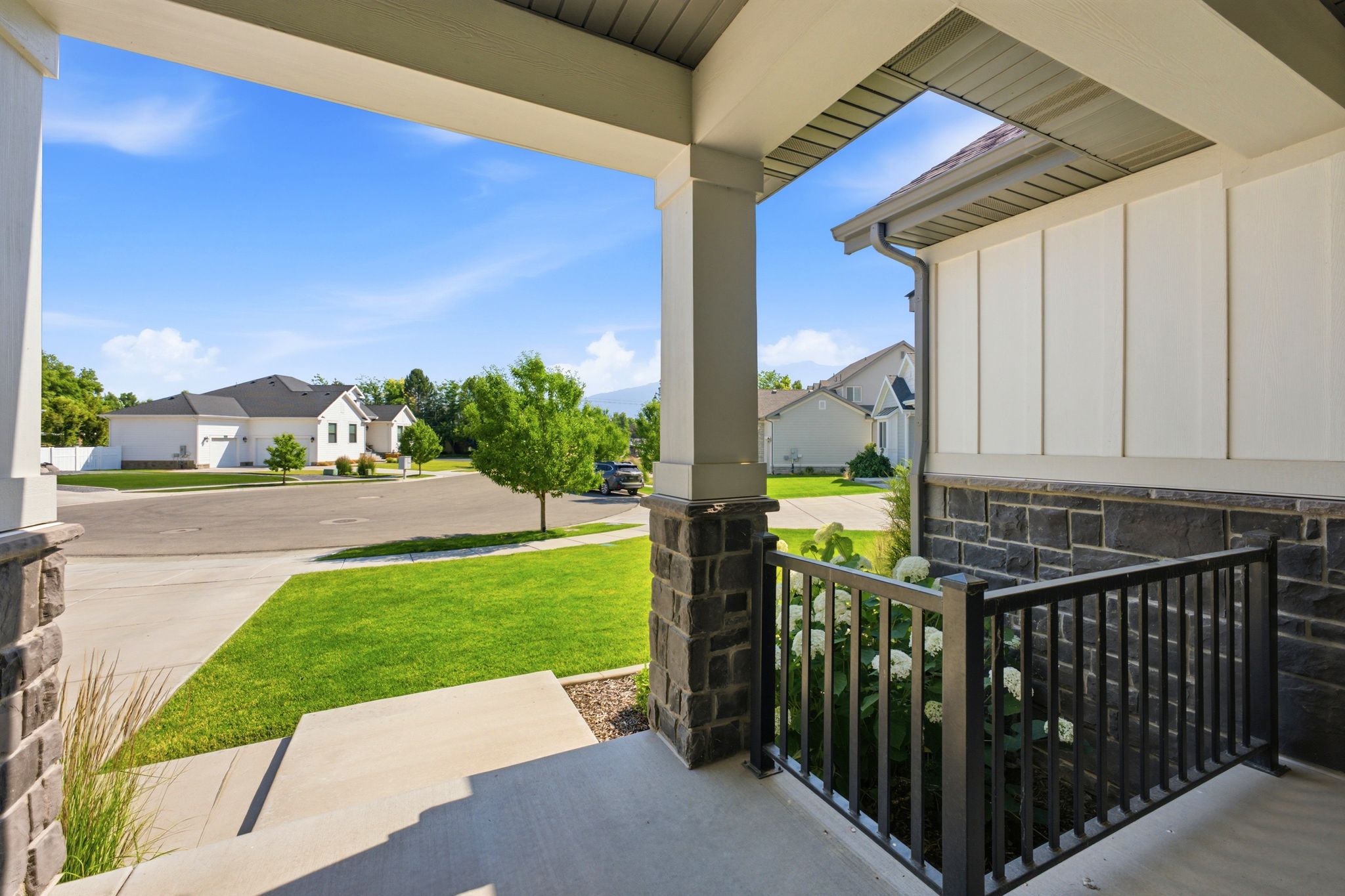 Covered porch entry featuring stone columns, white vertical siding, and a black metal railing