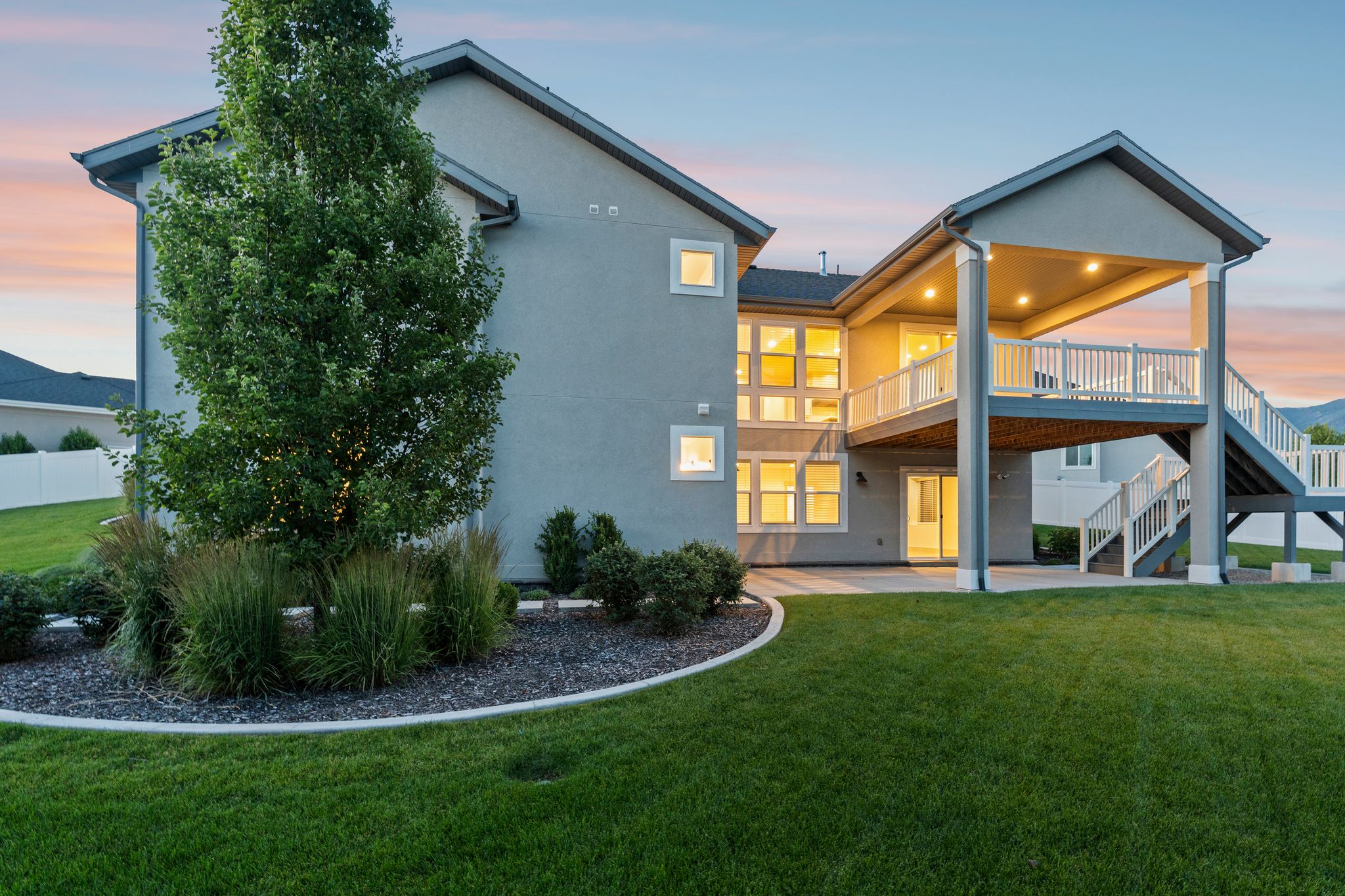 Rear exterior featuring a covered deck with white railing, recessed lighting, and stairs descending to a concrete patio