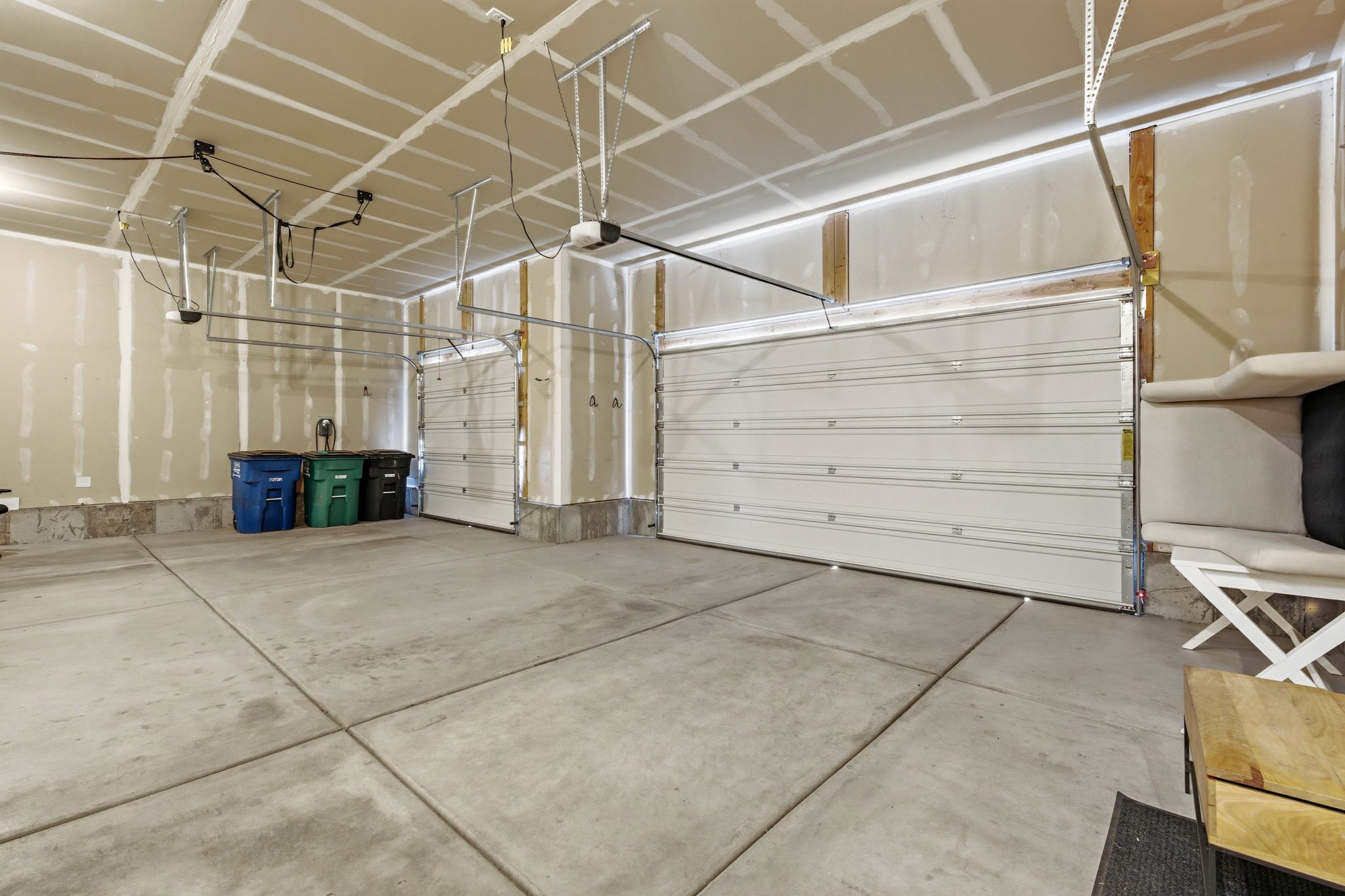 Spacious garage featuring a concrete floor, two white panel garage doors with openers, and unfinished drywall walls