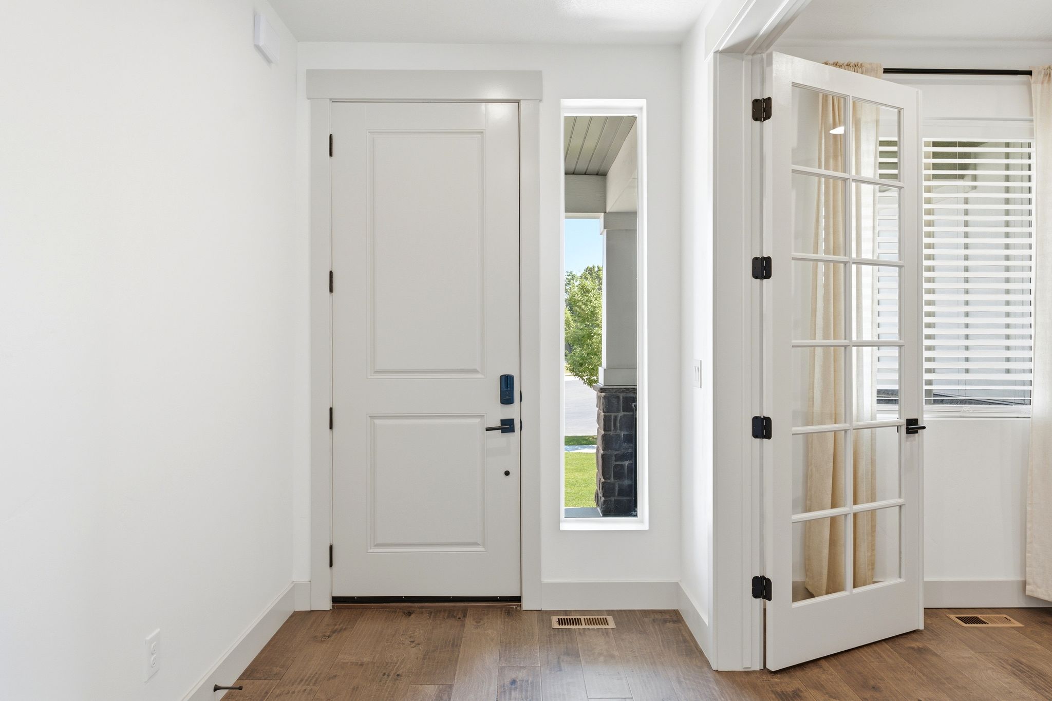 Entryway featuring wood-finish flooring, a white paneled entry door with black hardware, and an adjacent sidelight