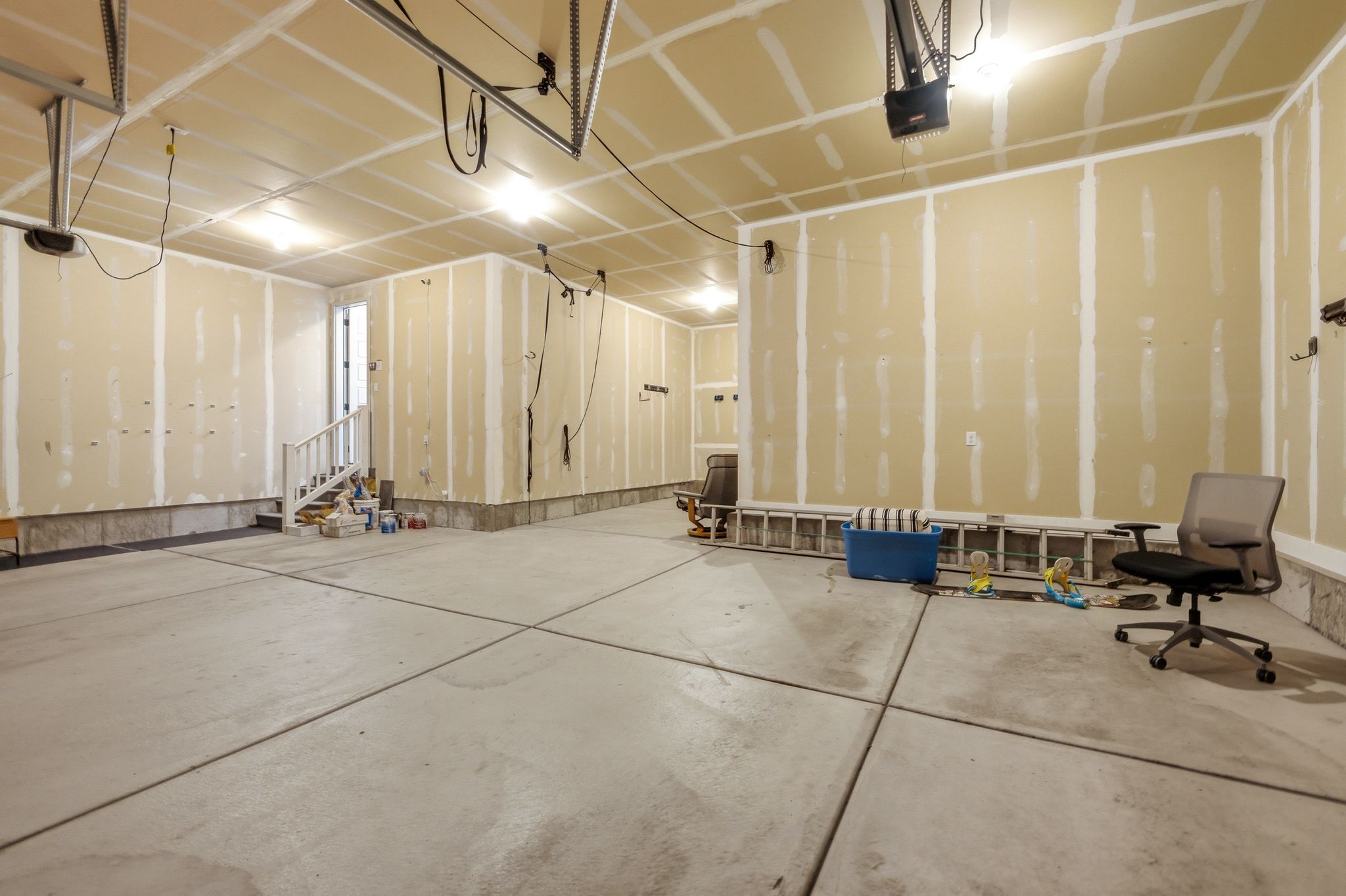 Spacious garage with exposed drywall, concrete flooring, and an interior staircase