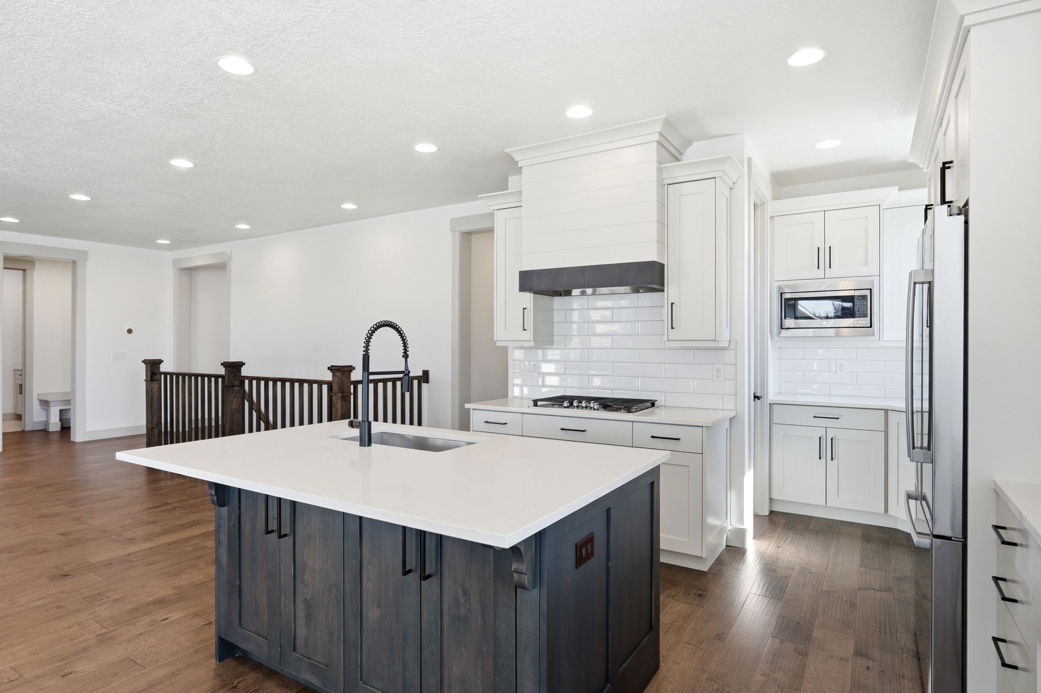 Modern kitchen featuring a dark wood-finish island with a white countertop and built-in sink, white cabinetry, subway tile backsplash, and stainless steel appliances