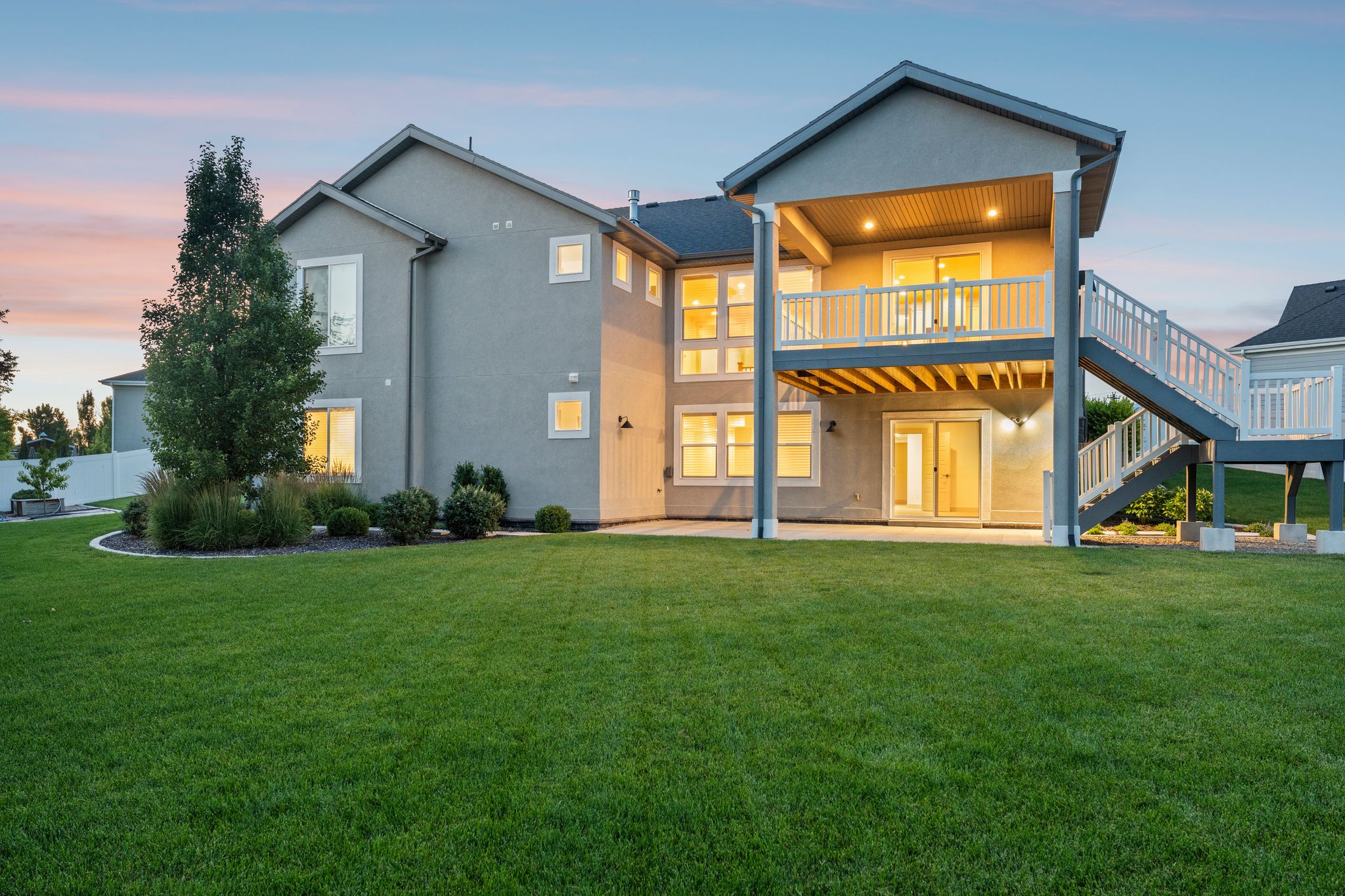 Spacious backyard featuring a two-story deck, ground-level patio, expansive lawn, and mature landscaping