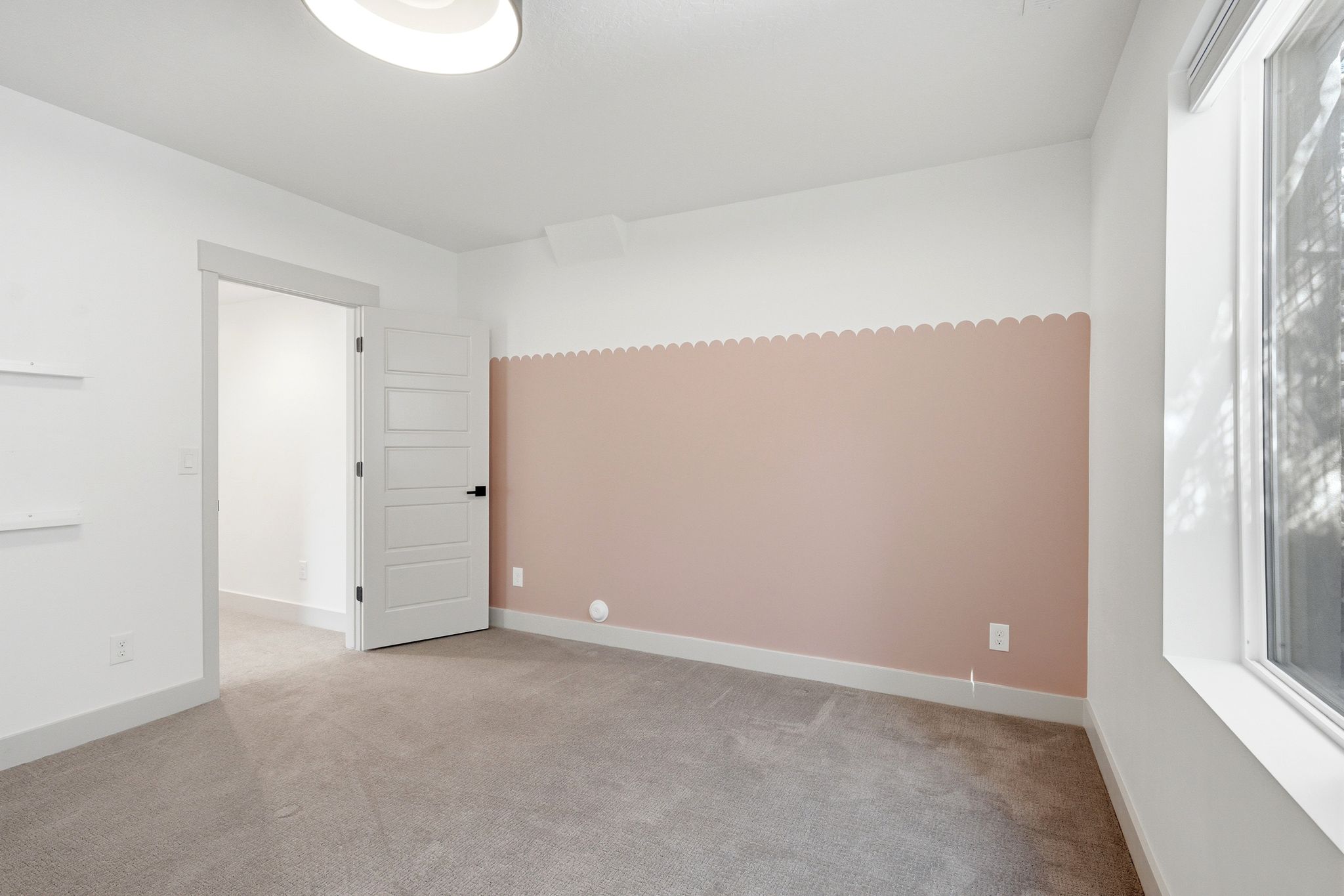 Carpeted room featuring a window, built-in shelving, a modern flush-mount ceiling light, and a five-panel door with matte black hardware