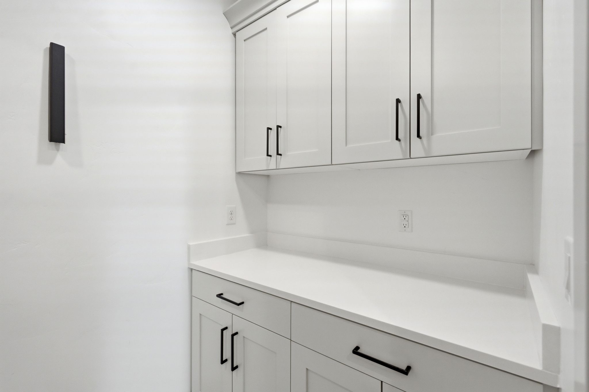 White shaker-style cabinetry with matte black hardware, solid surface countertops, and a white backsplash