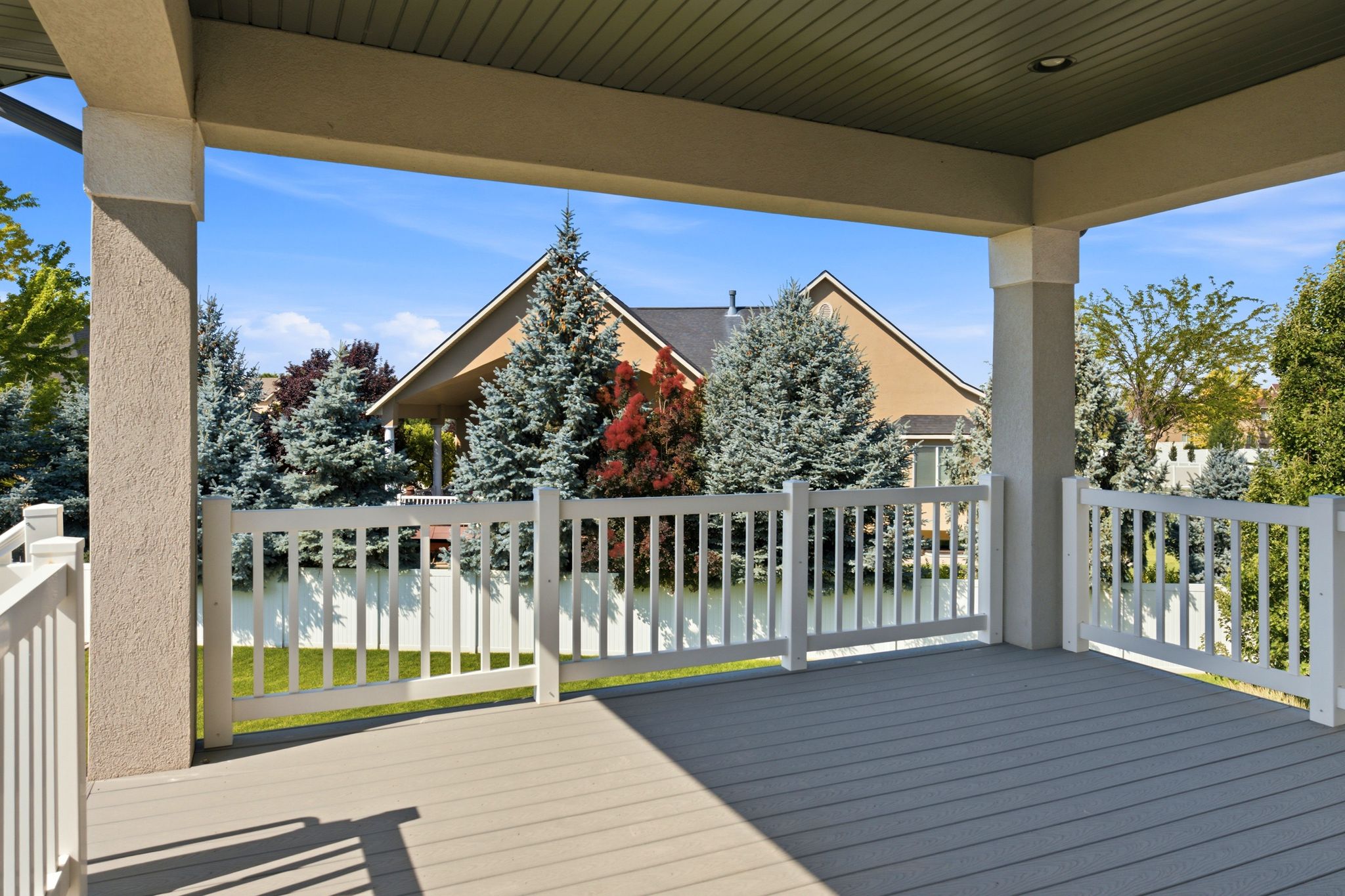 Covered patio featuring composite decking, stucco columns, white railing, and a tongue-and-groove ceiling with recessed lighting