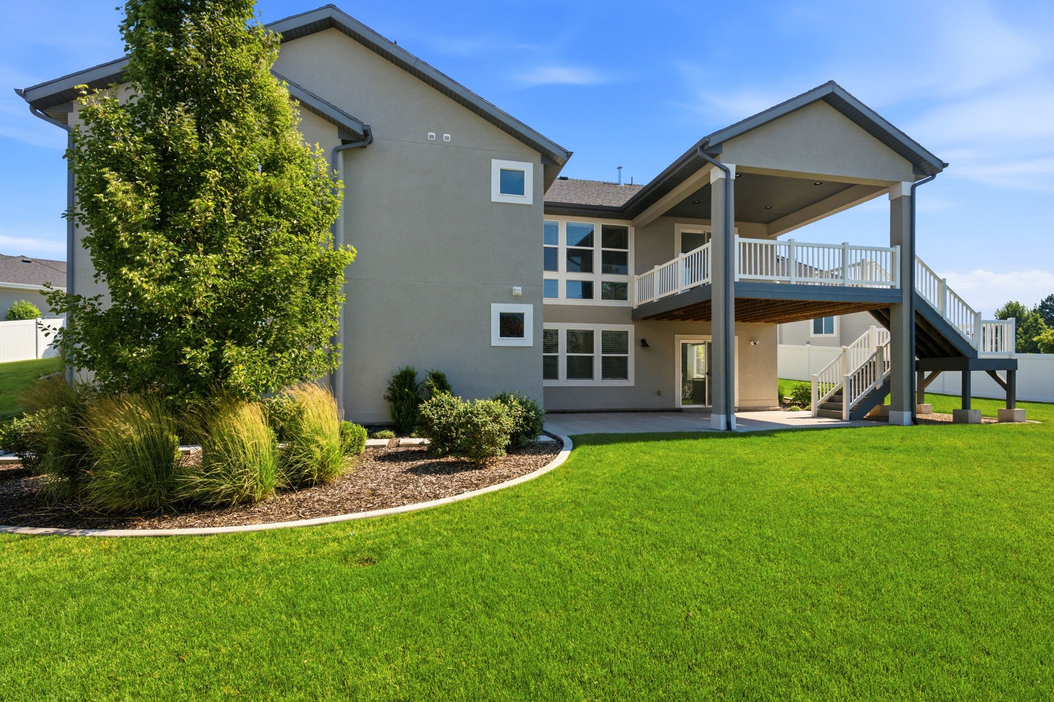 Rear exterior featuring a covered upper deck with white railings, a lower covered patio, and an expansive lawn