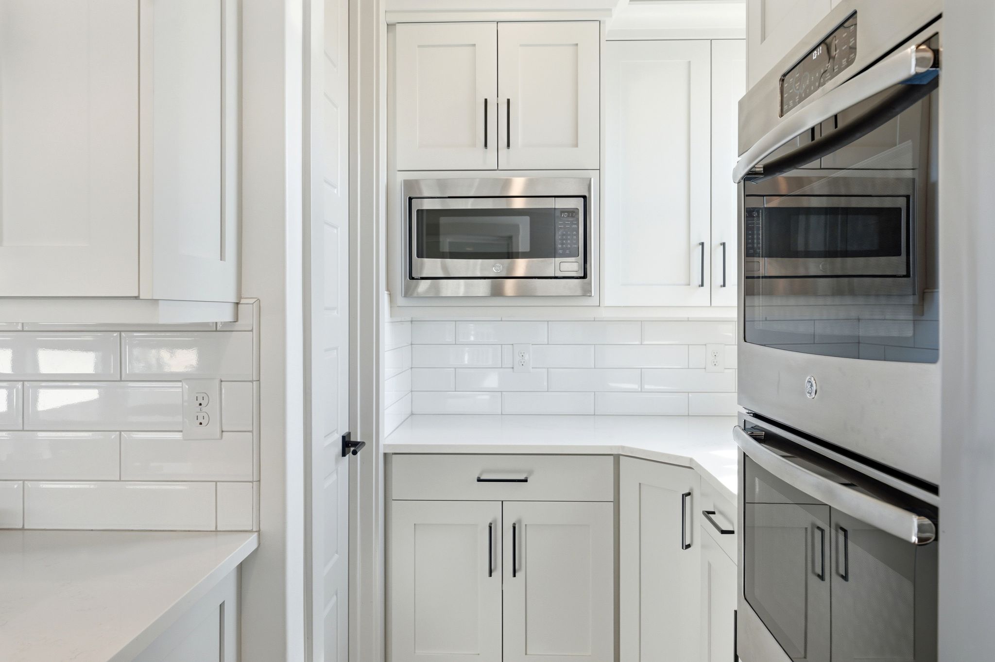 Modern kitchen featuring crisp white cabinetry, built-in stainless steel appliances, a subway tile backsplash, and light-toned countertops