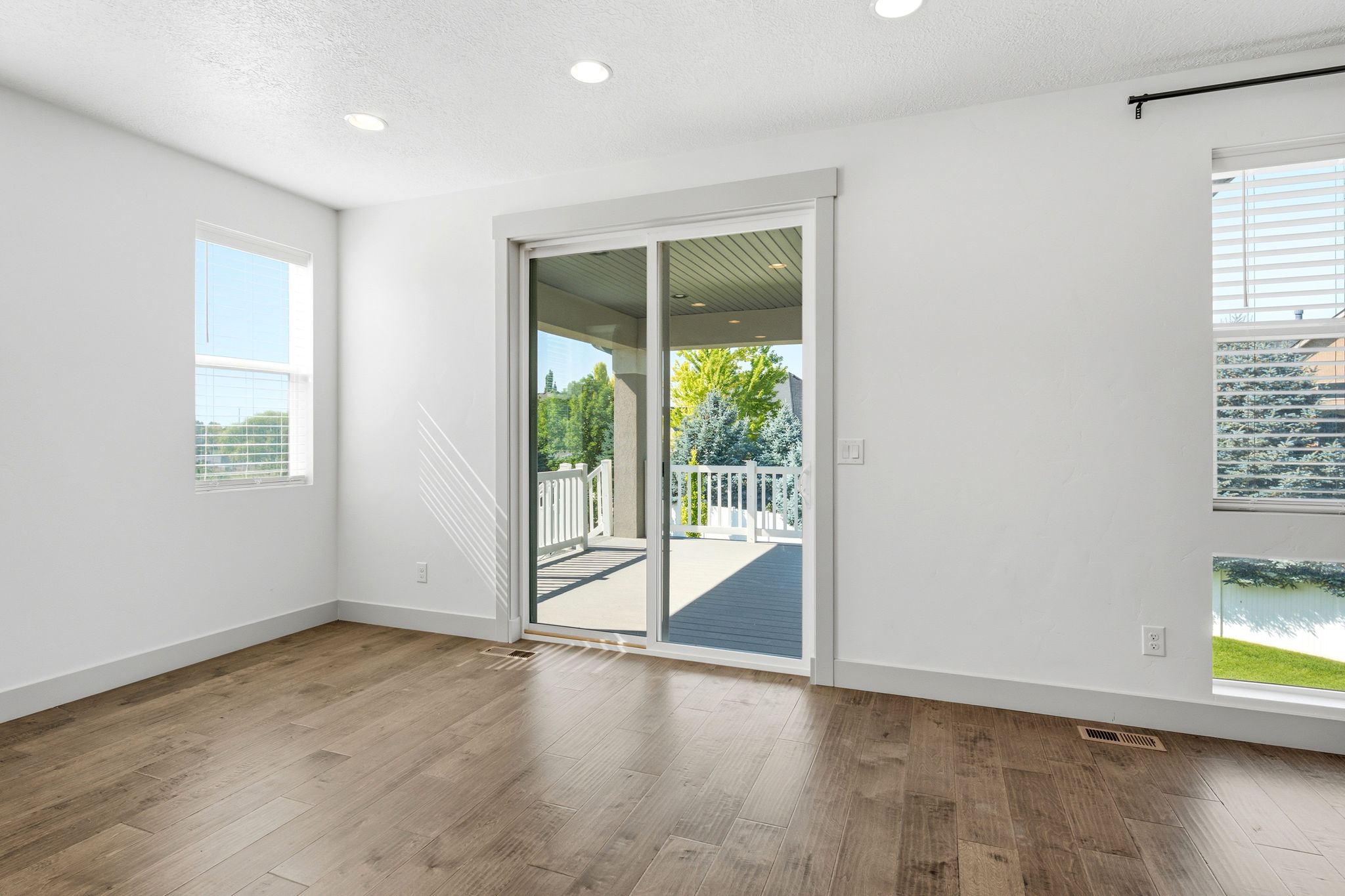 Spacious room featuring wood-finish flooring, recessed lighting, and a sliding glass door leading to an outdoor deck with white railings