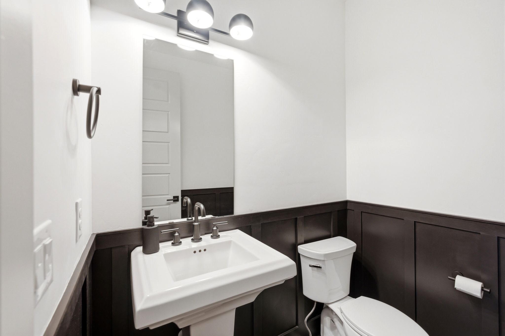 Pedestal sink with bronze-finish faucet, framed mirror, and three-light vanity fixture