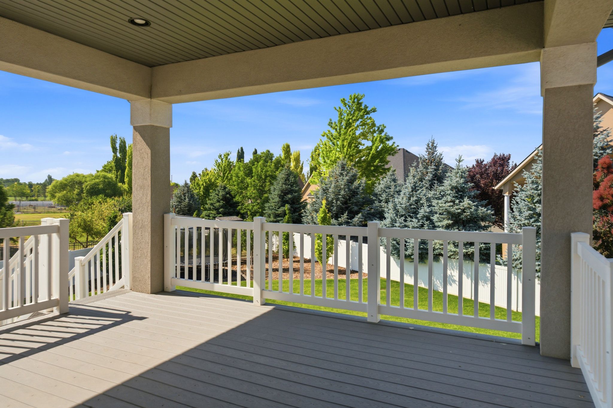 Expansive covered deck featuring composite decking, white railing, recessed lighting, and stucco support columns