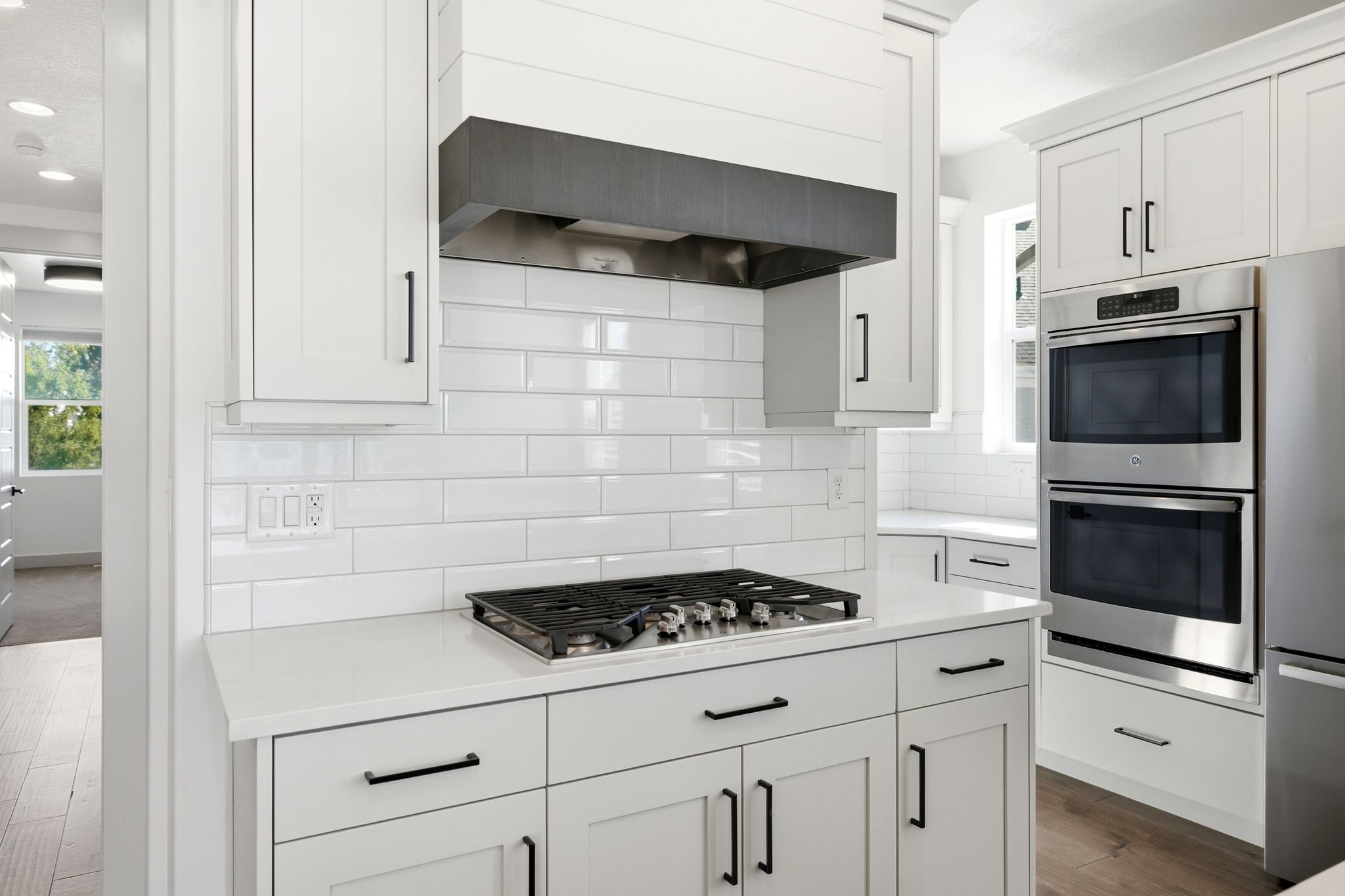Modern kitchen featuring a gas cooktop, built-in double ovens, white shaker cabinetry with matte black hardware, white subway tile backsplash, and light-toned countertops