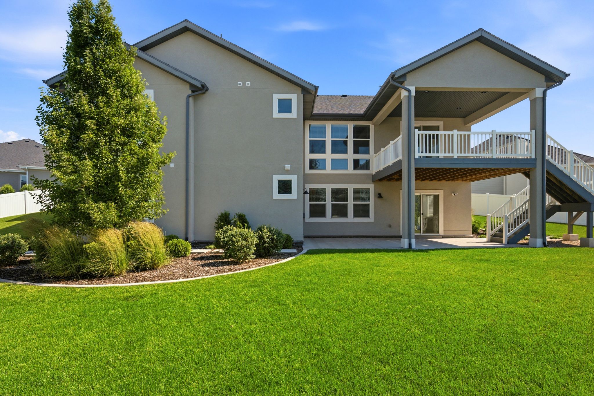 Rear exterior featuring a covered upper-level deck with white railings, a lower-level concrete patio, and a sliding glass door entry
