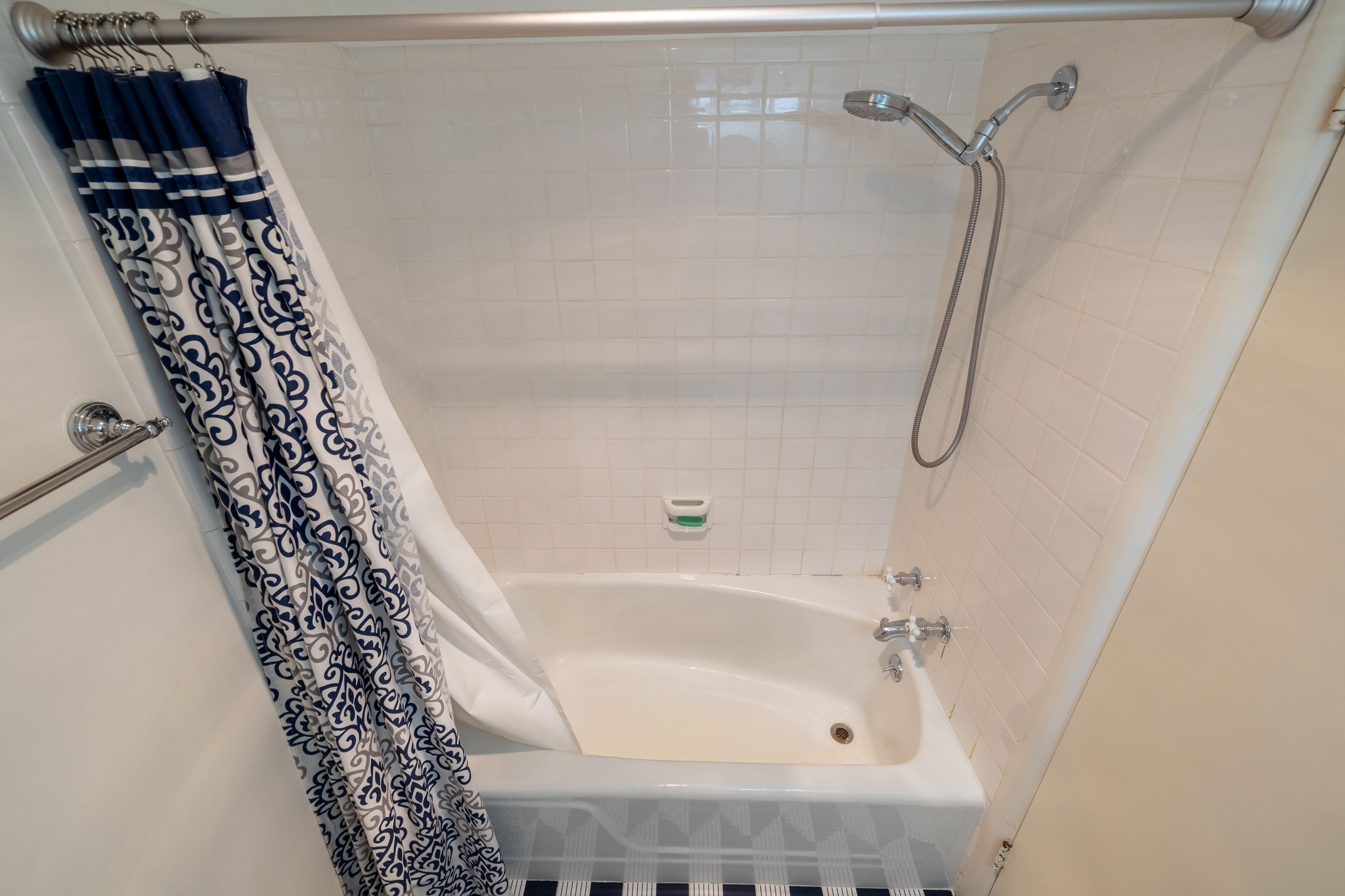 Bathtub and shower combination featuring white subway tile surround, polished chrome fixtures, and a curved shower rod