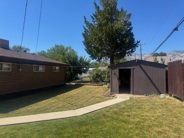 Expansive backyard featuring a manicured lawn, concrete pathway, and a brown wood-paneled storage shed