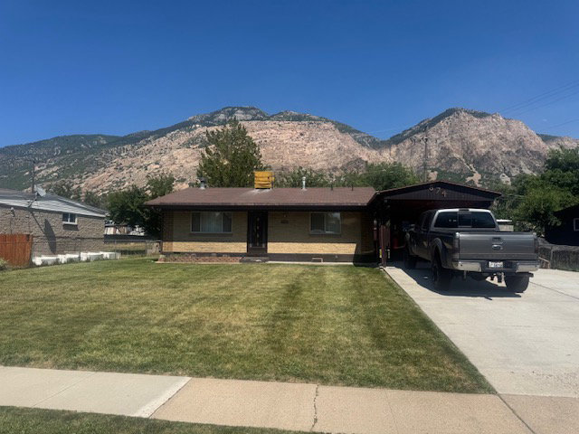Exterior featuring a landscaped front lawn, a paved driveway, and an attached carport