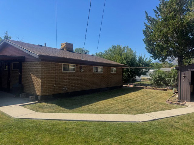 Expansive lawn area featuring a concrete pathway, a brick exterior, a shed, mature trees, and a mountain backdrop