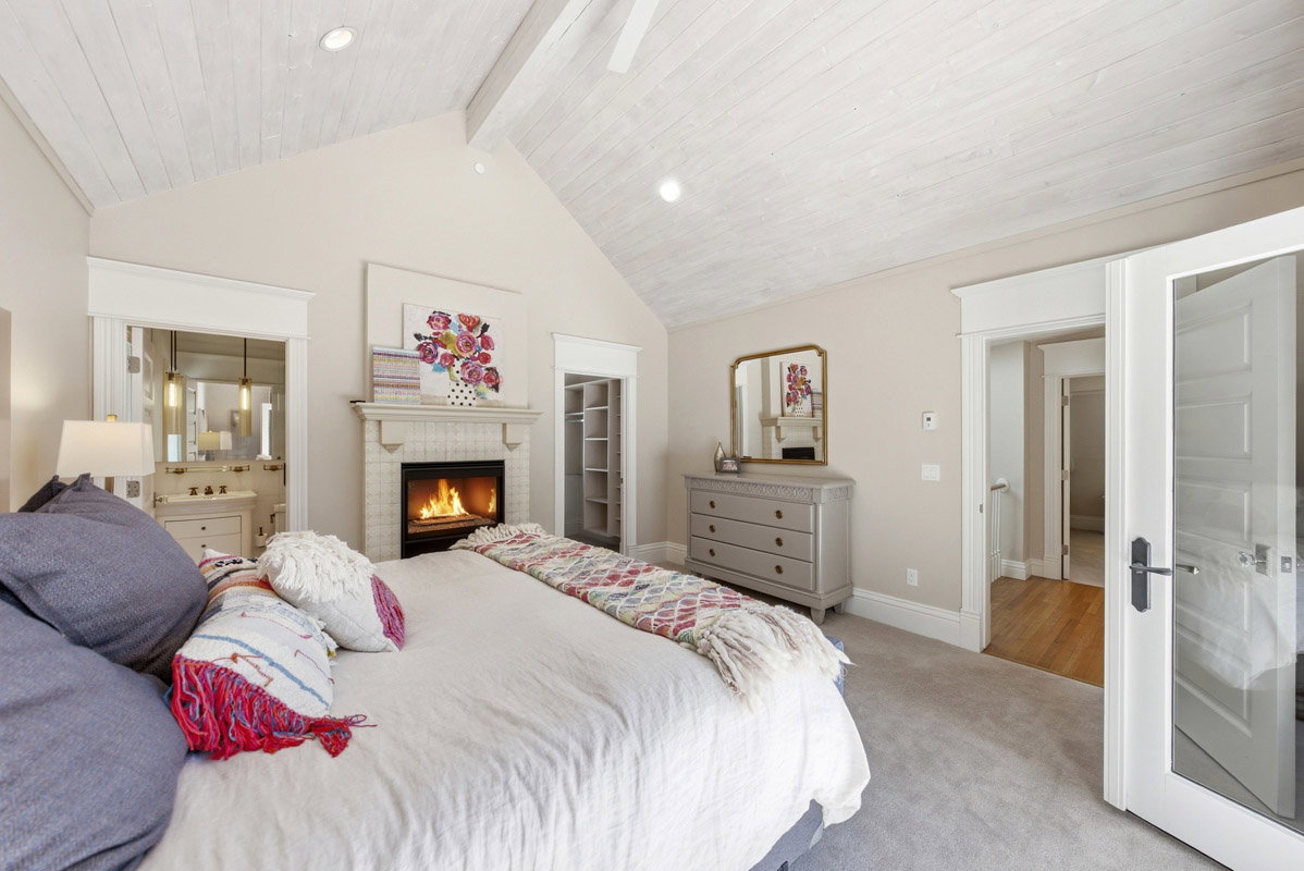 Vaulted ceiling with white wood-paneling, fireplace with tile surround, carpeted flooring, and a built-in shelving unit