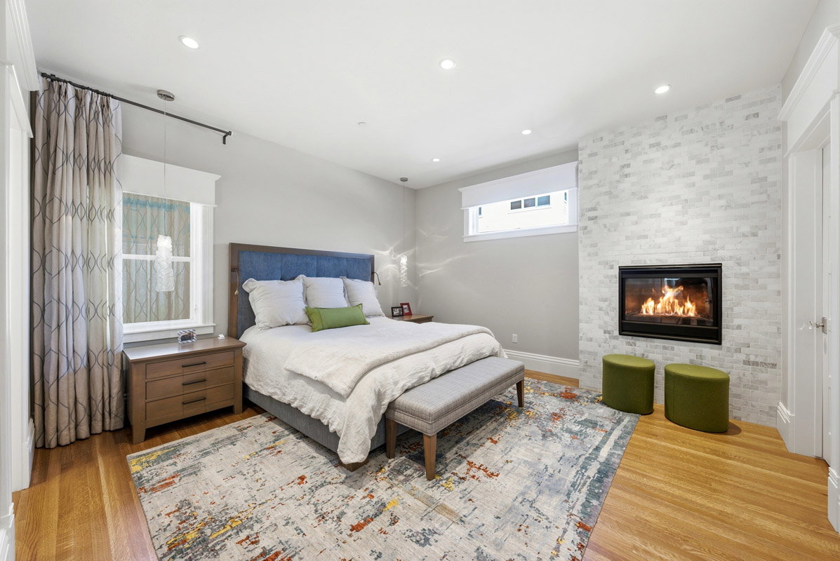 Recessed lighting illuminates this room featuring wood-finish flooring, a white brick-patterned fireplace with black trim, and a window with white trim