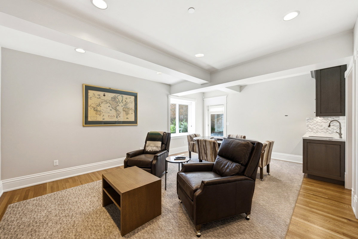Finished basement space featuring recessed lighting, a built-in wet bar with white countertop and wave-patterned tile backsplash, multiple windows, and a combination of carpet and wood-finish flooring