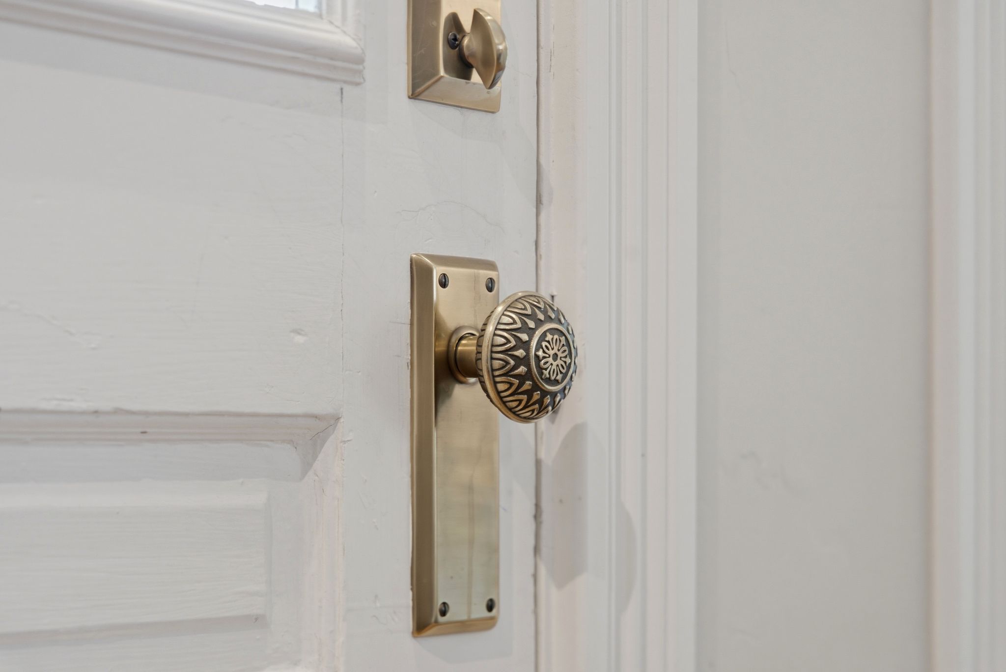 White paneled door with an ornate brass doorknob and matching escutcheon plate
