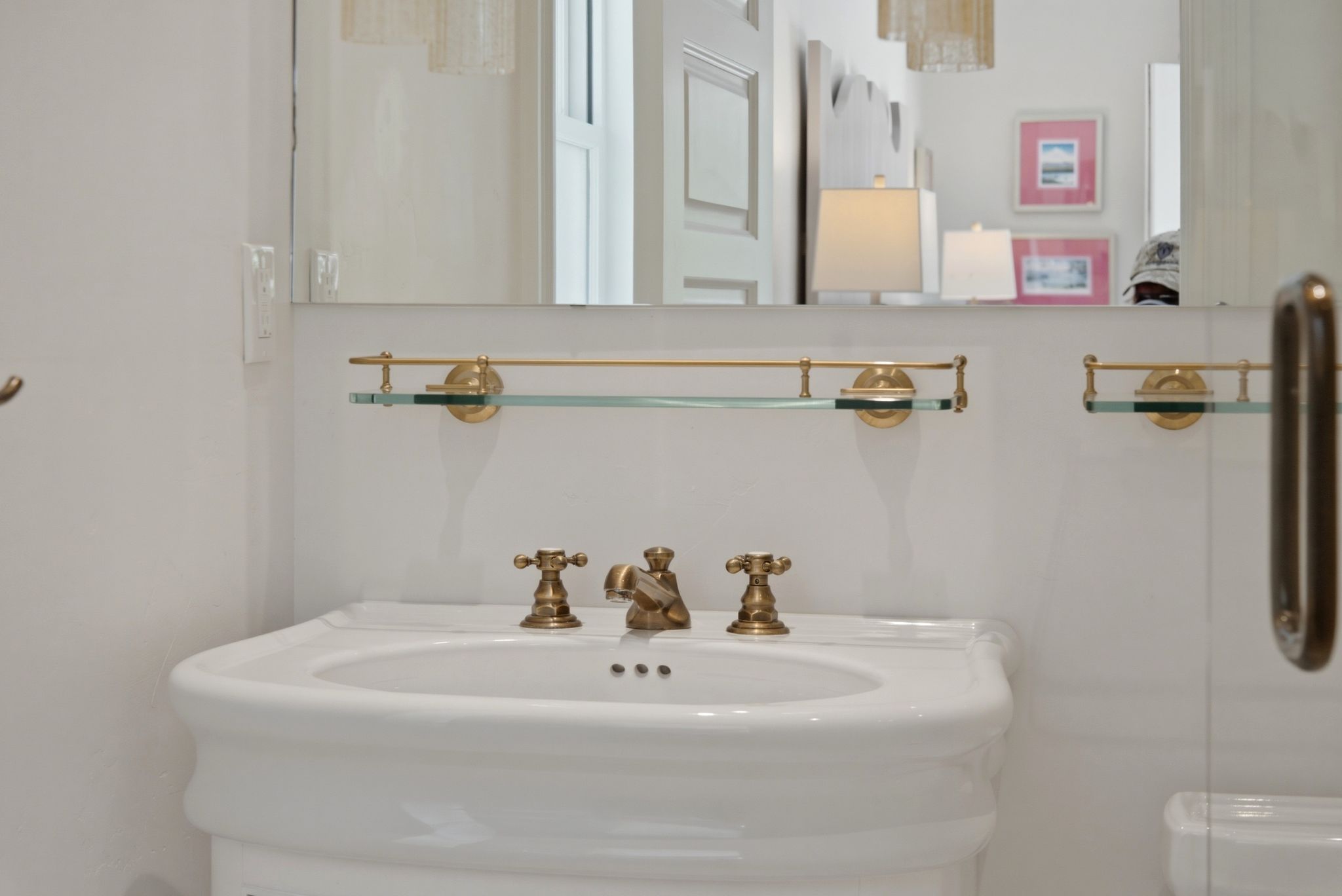 White pedestal sink with antique brass faucet and fixtures, featuring a wall-mounted glass shelf