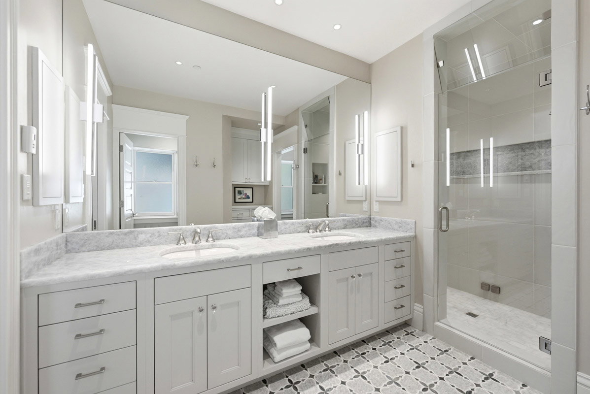 Dual vanity with undermount sinks, stone countertop, custom cabinetry, and patterned floor tile
