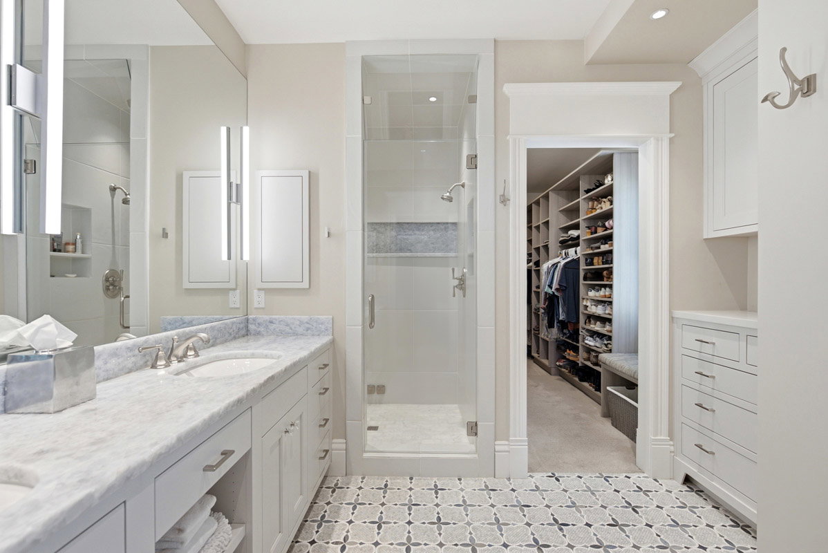 Bathroom featuring a dual-sink vanity with a stone countertop, a glass-enclosed shower, built-in cabinetry, and patterned floor tile