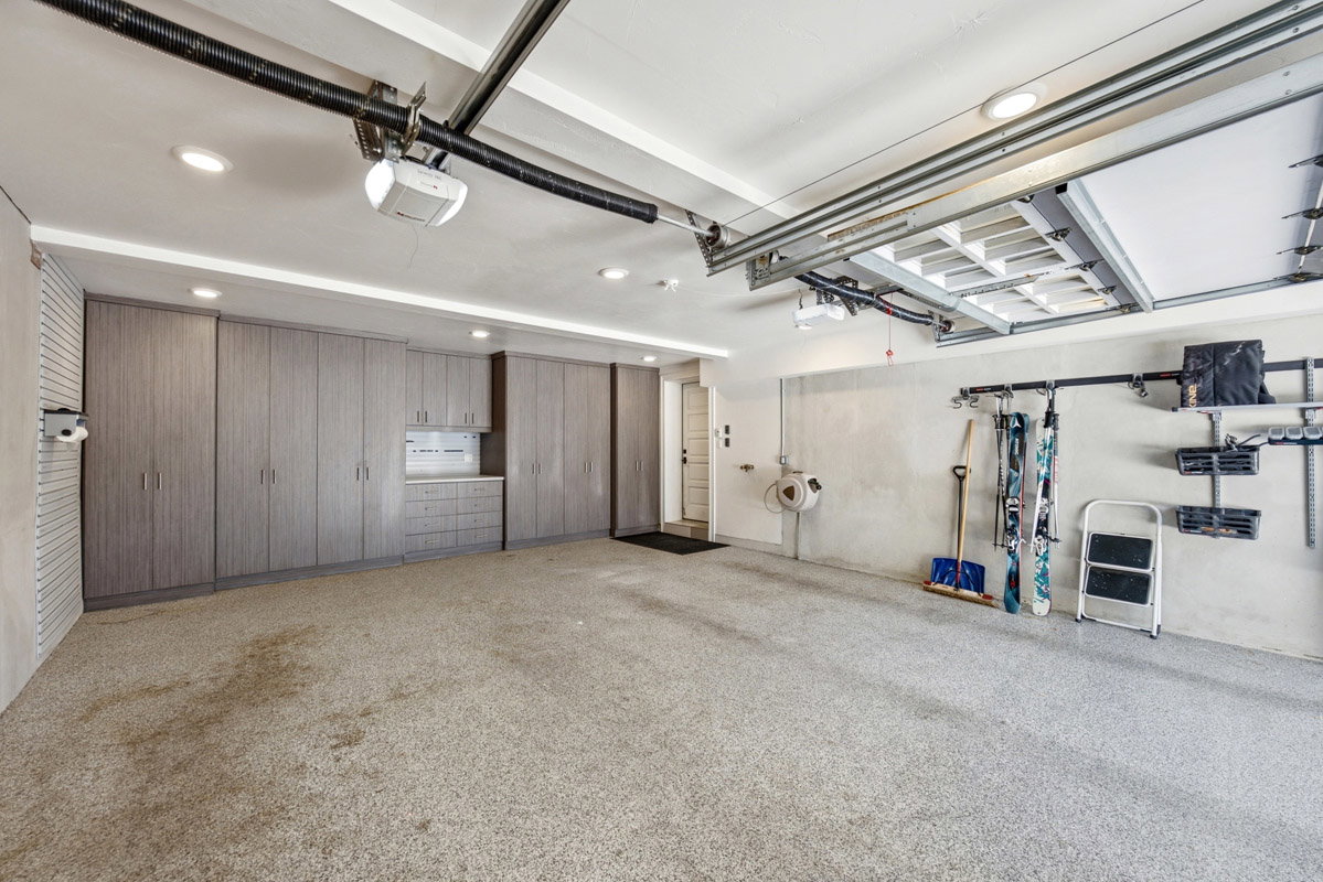 Spacious garage featuring extensive built-in cabinetry, overhead lighting, epoxy flooring, and wall-mounted organization systems