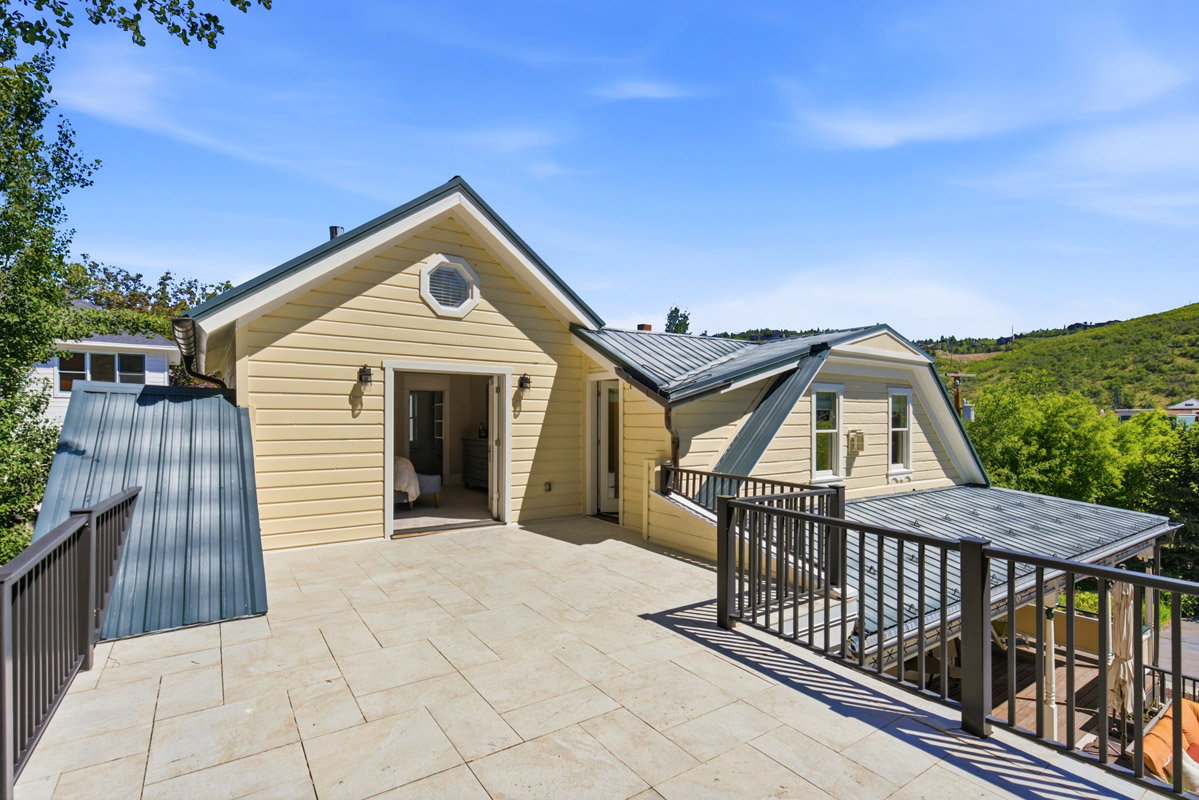 Expansive outdoor patio featuring light-toned tile flooring, metal railings, and direct access to an interior space via French doors