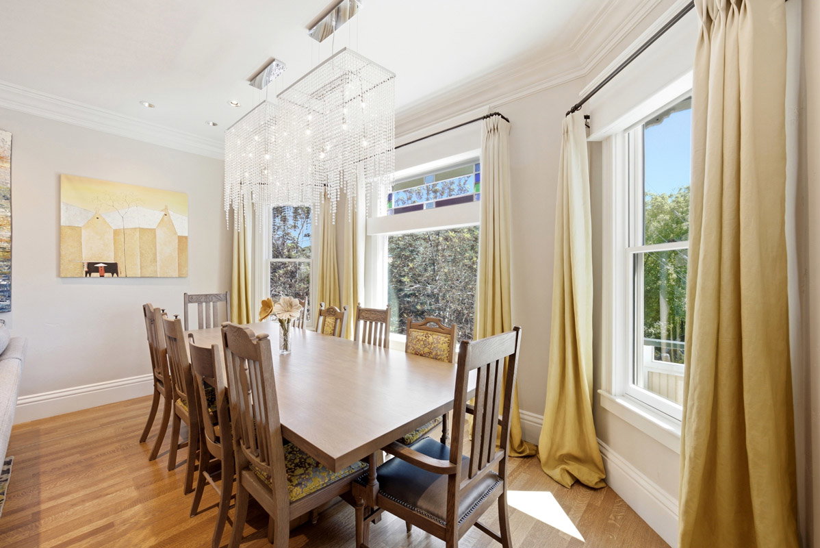 Dining area featuring wood-finish flooring, a rectangular crystal chandelier, and multiple pane windows with an upper stained glass accent