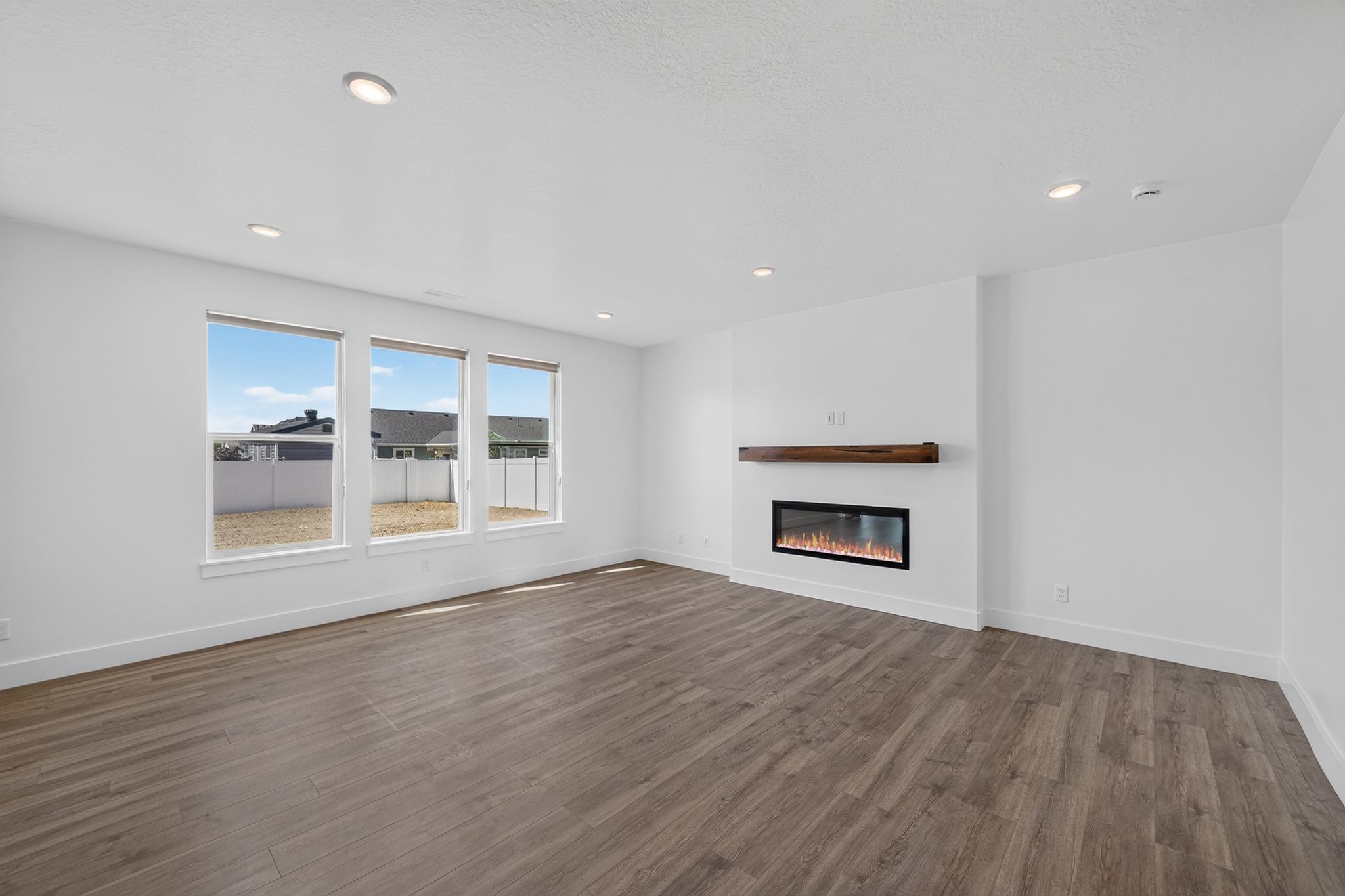 Spacious room featuring wood-finish flooring, recessed lighting, and a built-in electric fireplace with a wood mantle