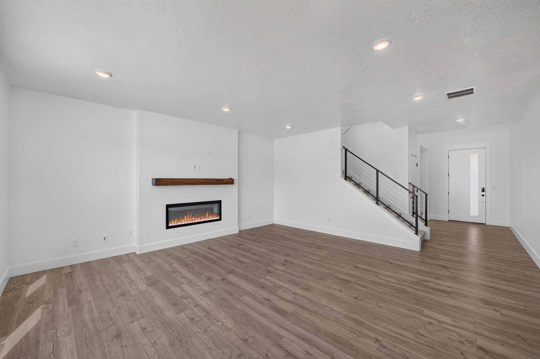 Open-concept living space featuring wood-finish flooring, recessed lighting, and an electric fireplace with a wood mantel