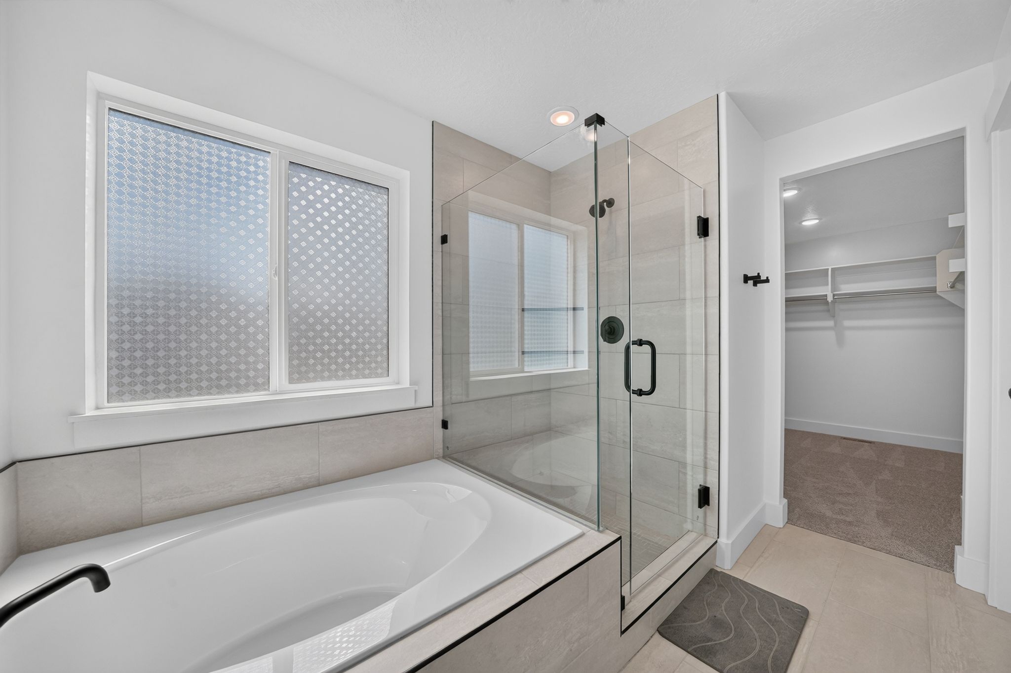 Contemporary primary bathroom featuring a built-in soaking tub with matte black fixtures, a glass-enclosed shower, and light-toned tile flooring