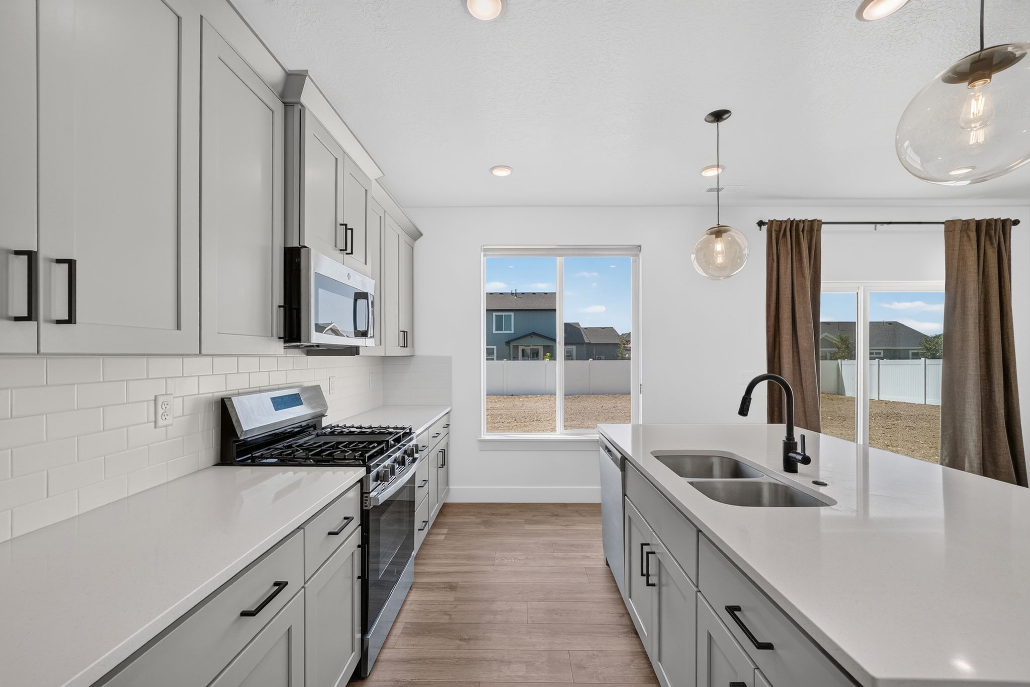 Modern kitchen featuring light gray cabinetry, white countertops, stainless steel appliances, and wood-finish flooring