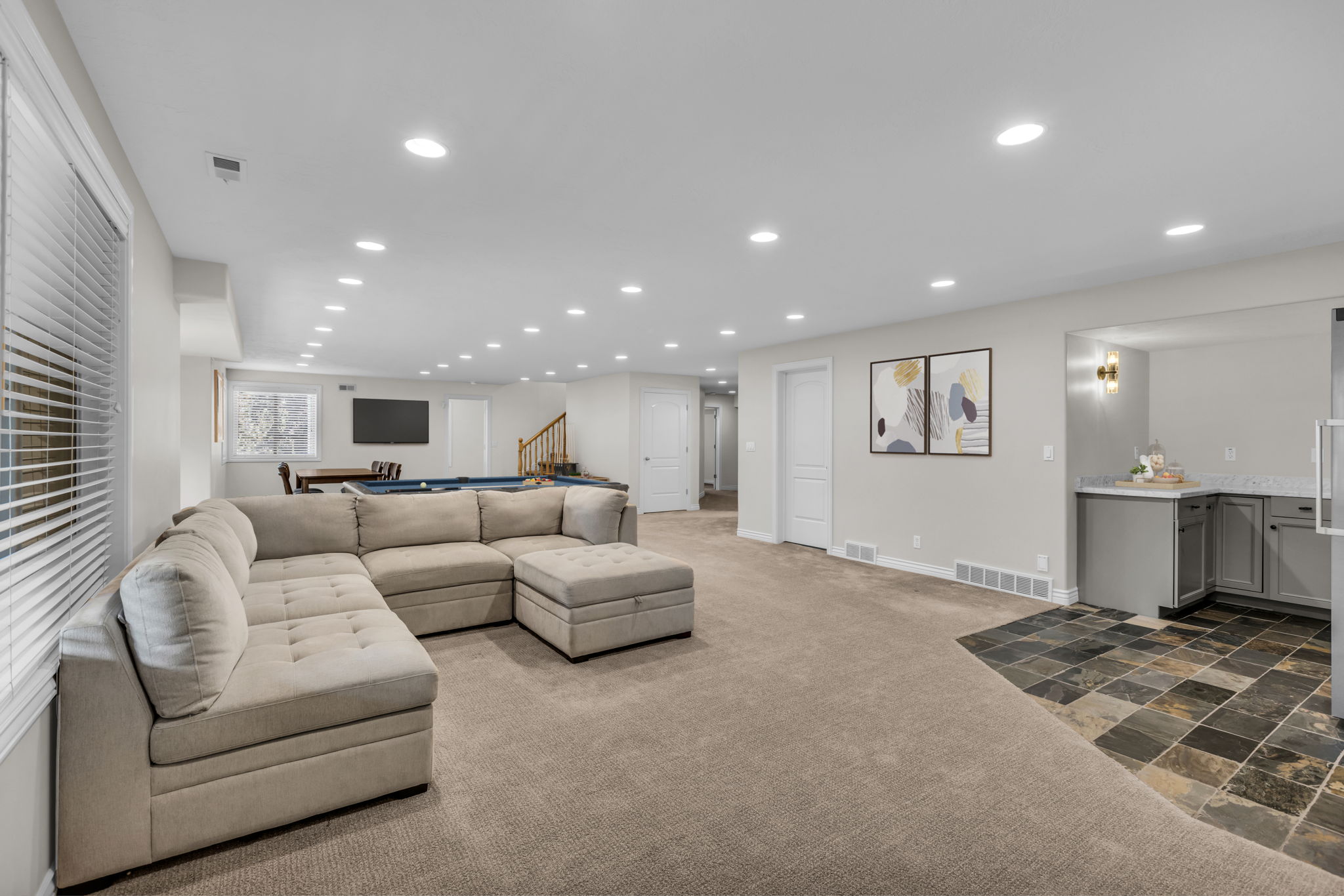 Spacious recreation room featuring recessed lighting, a built-in wet bar with gray cabinetry and stone-finish countertops, and a distinct slate-tile floor section