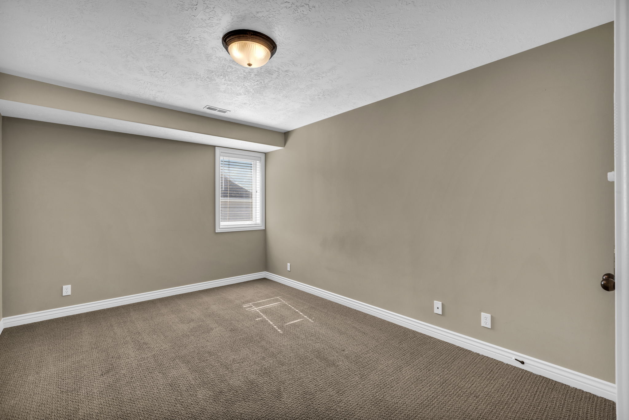 Carpeted room featuring a single window with blinds, a ceiling-mounted light fixture, white baseboards, and neutral wall paint